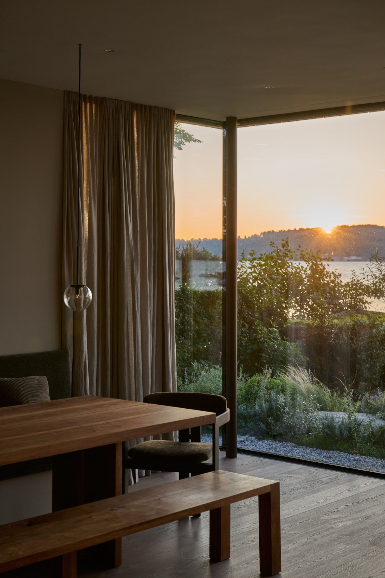 Stimmungsvoller Essbereich mit bodentiefen Fenstern und warmem Abendlicht für ein naturnahes, beruhigend elegantes Wohnambiente.