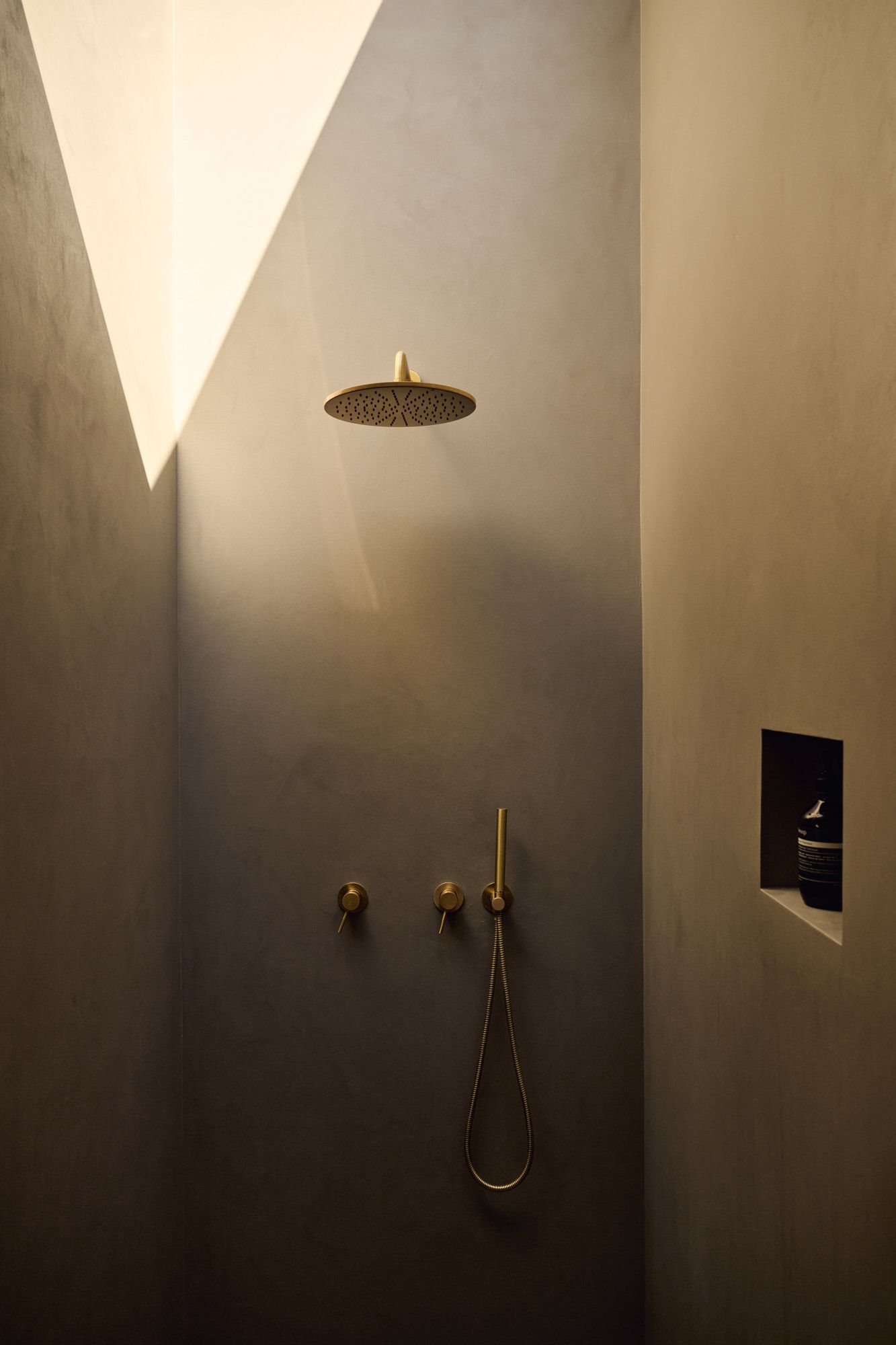 Minimalistische Walk-in-Dusche mit fugenlosen Wänden und goldenen Armaturen für ein warmes, modernes Spa-Ambiente.