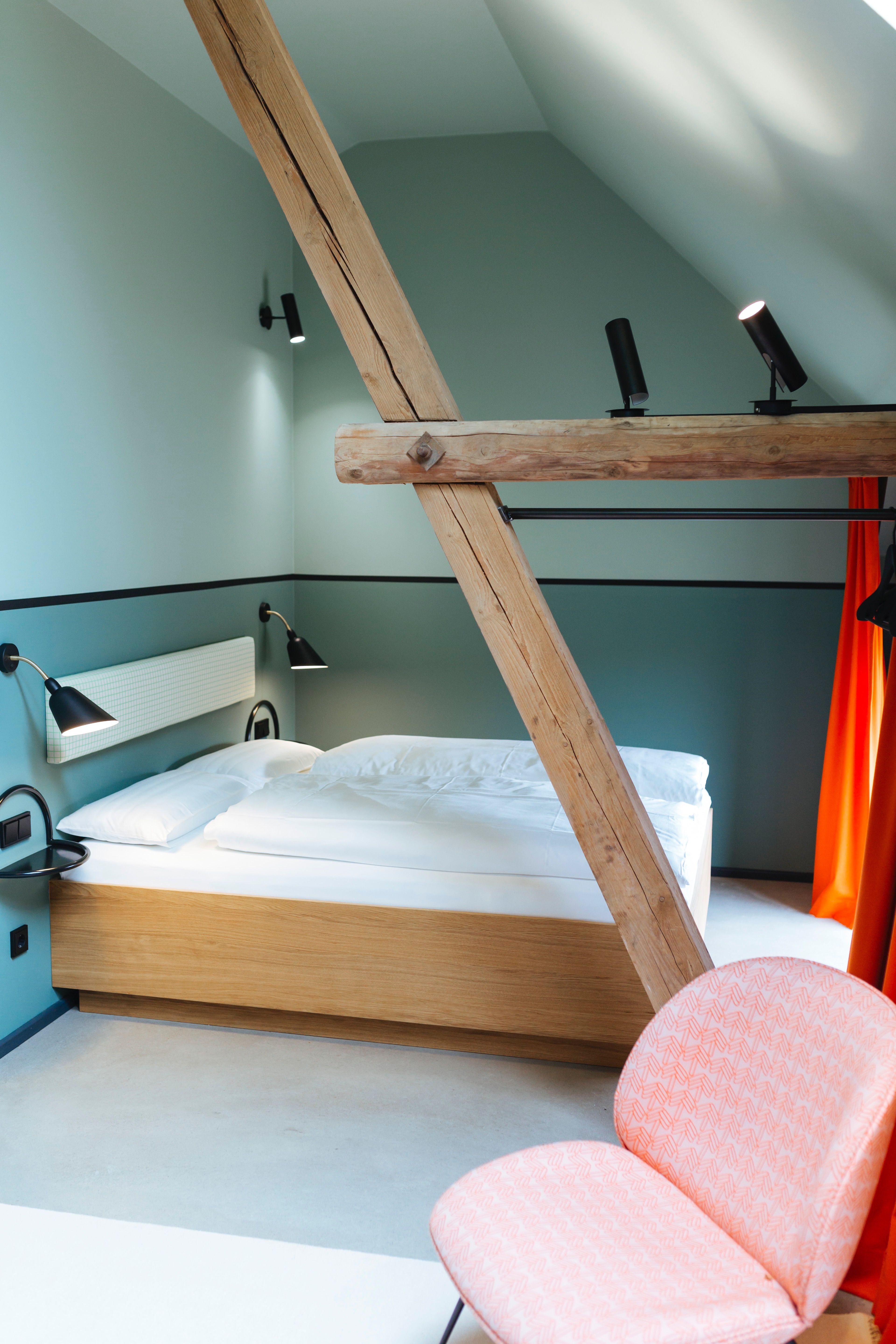 Das Schlafzimmer mit Holzbett, sichtbarer Dachkonstruktion und akzentuierter Beleuchtung ist ein charakteristisches Element des Hotels Kloster Möllenbeck.