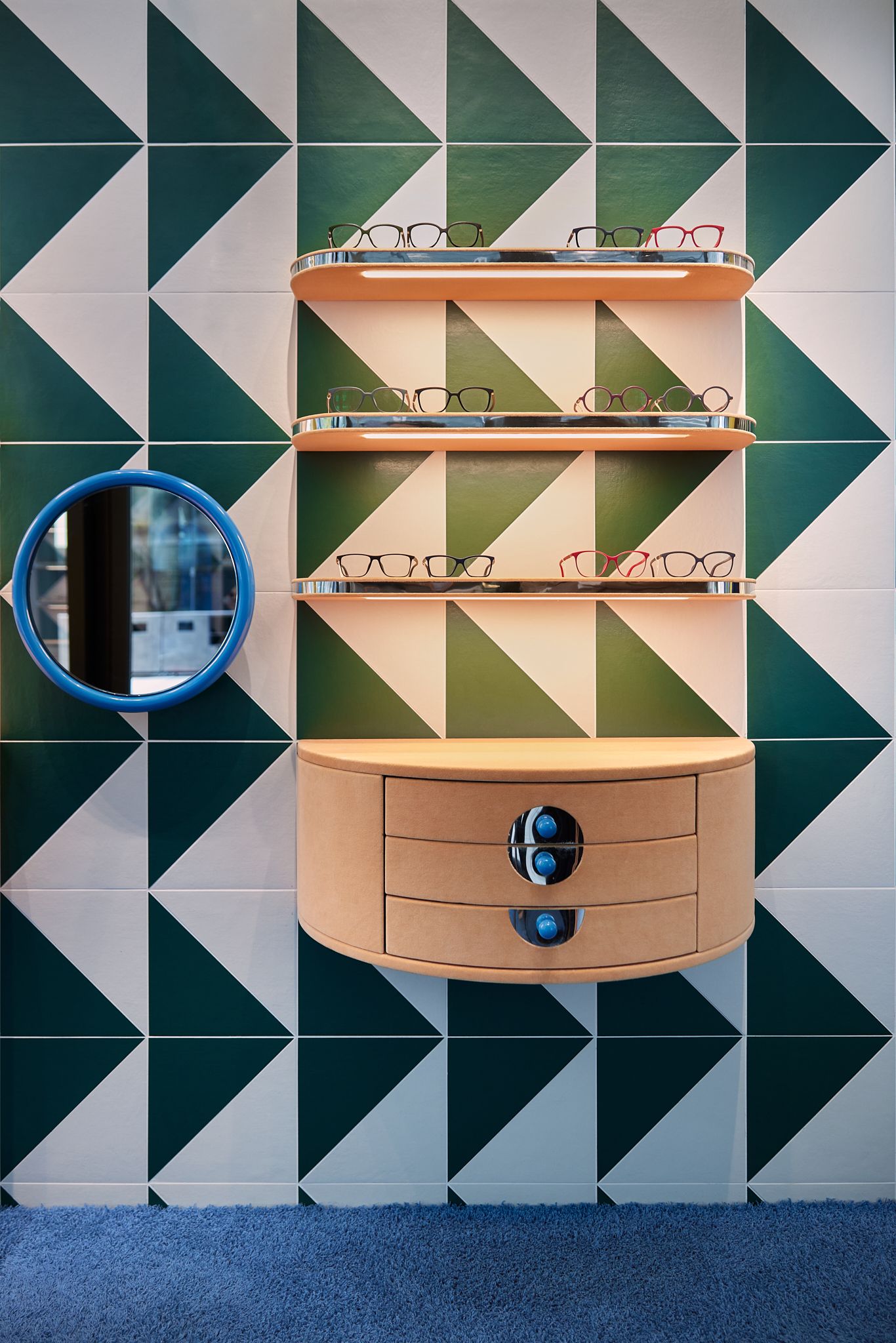 Das präzise gestaltete Regalsystem mit organischer Formensprache und klarer Linienführung präsentiert Kinderbrillen vor einer auffälligen grafischen Fliesenwand – designt von Stephanie Thatenhorst für Rookies Eyewear for Kids.