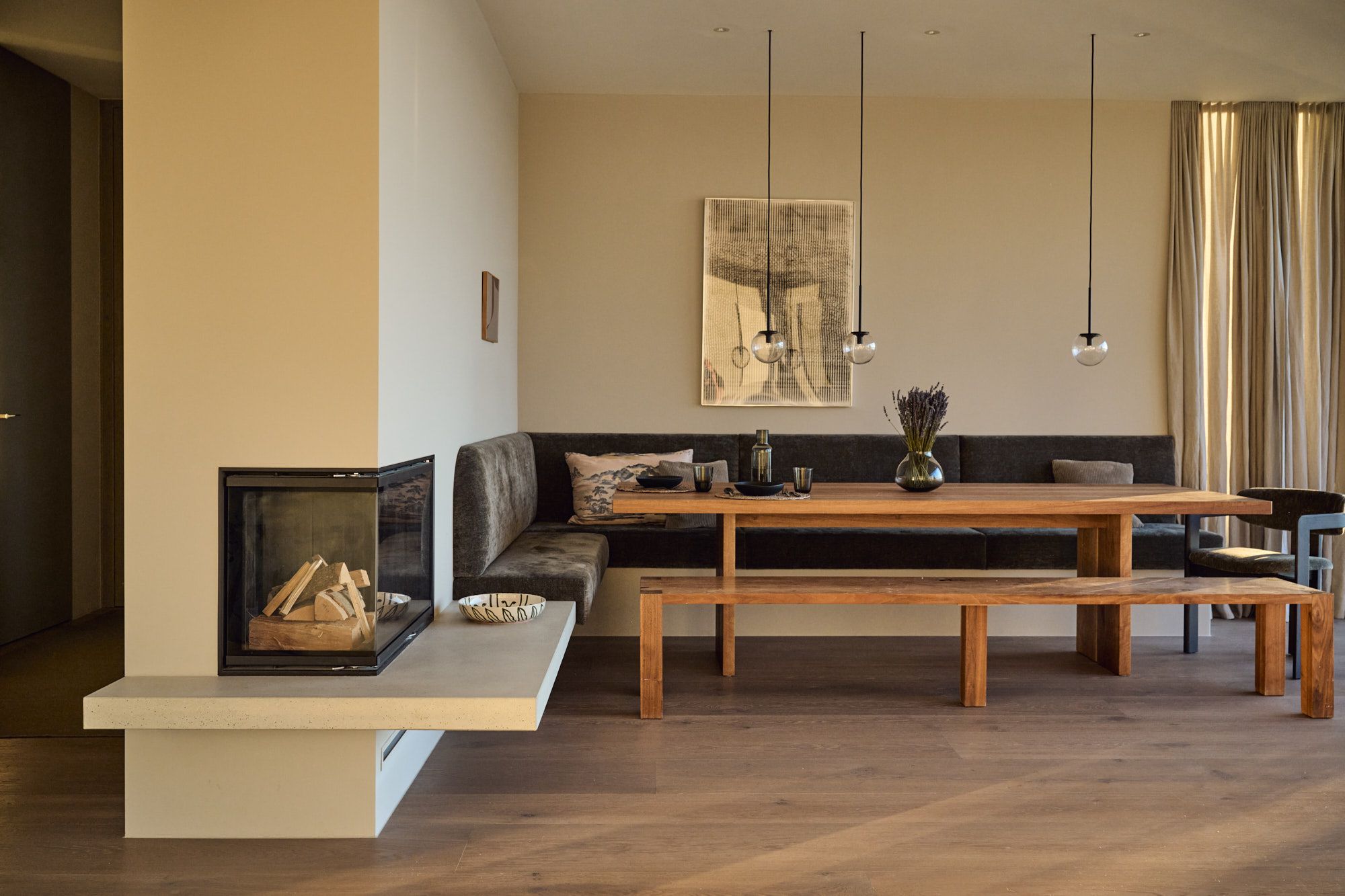 Warmer Essbereich mit maßgefertigter Sitzbank, massivem Holztisch und modernem Kamin für ein einladend elegantes Wohnambiente