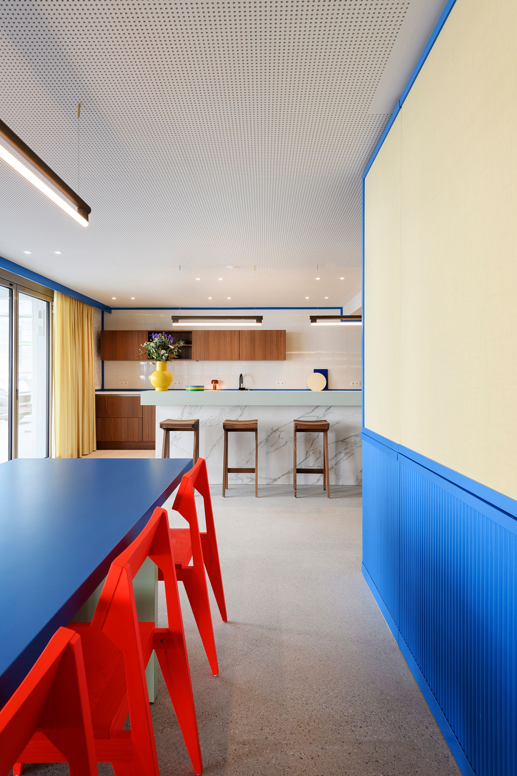 Der langgestreckte Esstisch mit kräftig blauen und roten Akzenten wurde von Stephanie Thatenhorst designt und setzt in der Kupa – Kitchen & Working Lounge ein ausdrucksstarkes