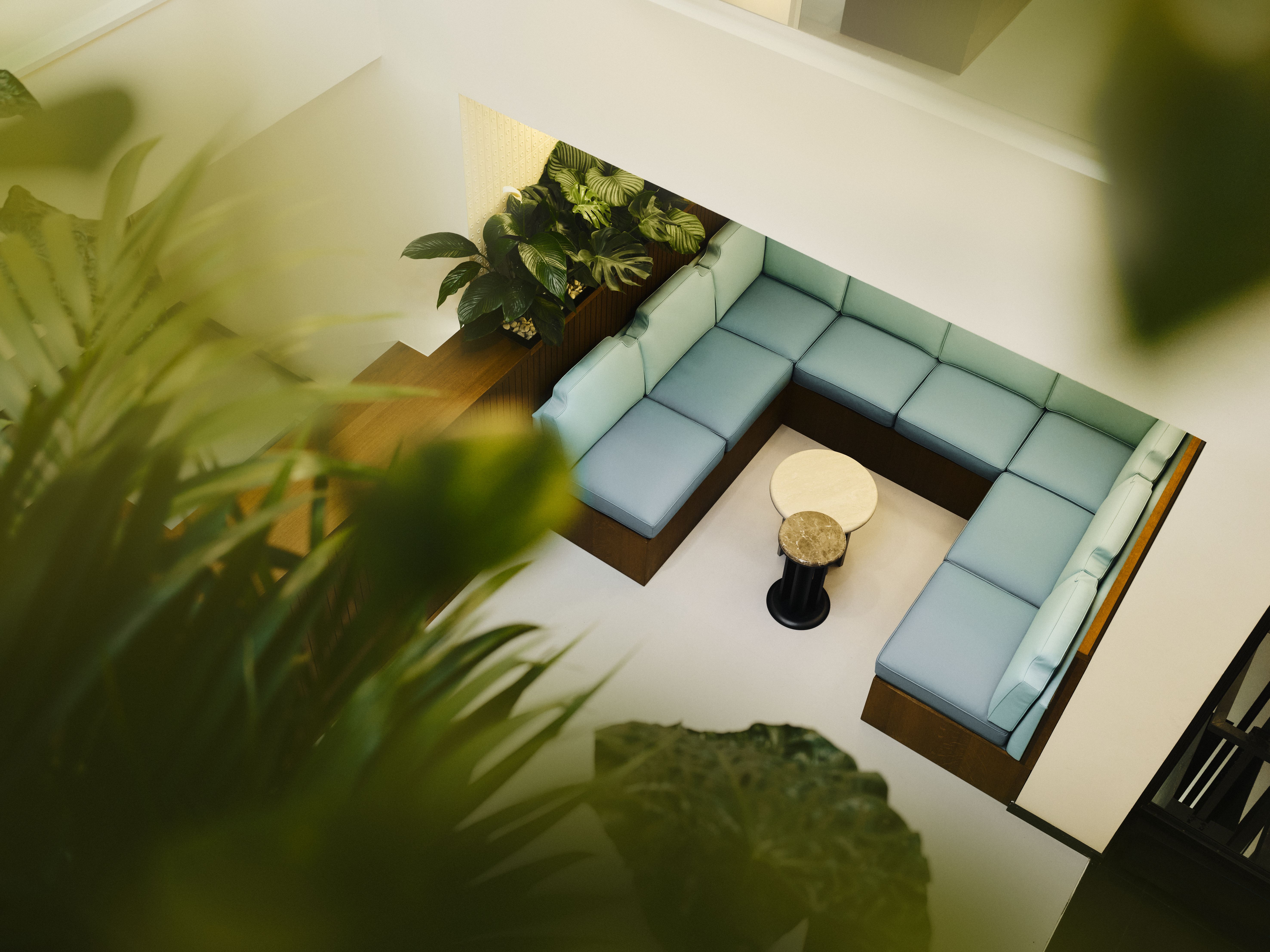 Die Community Area präsentiert eine großzügige Lounge mit umlaufender Sitzbank in softem Mint, üppigem Grün und eleganten Naturtönen, designed by Stephanie Thatenhorst.