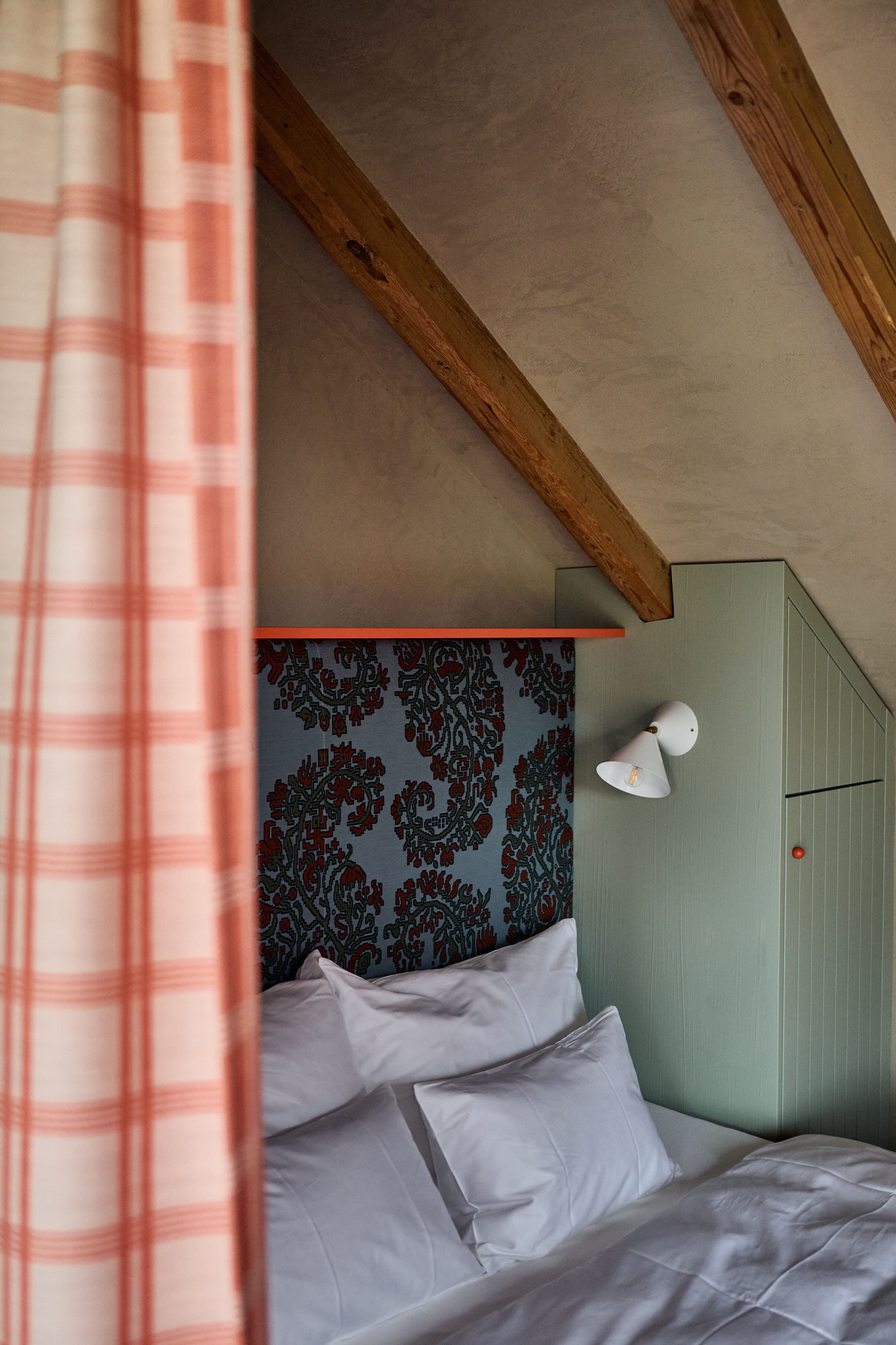 Schlafzimmer mit ornamentaler Stoffpaneel-Wand, pastellgrünem Einbauschrank und Vorhang in Alpen-Karomuster als harmonische Farbkomposition.