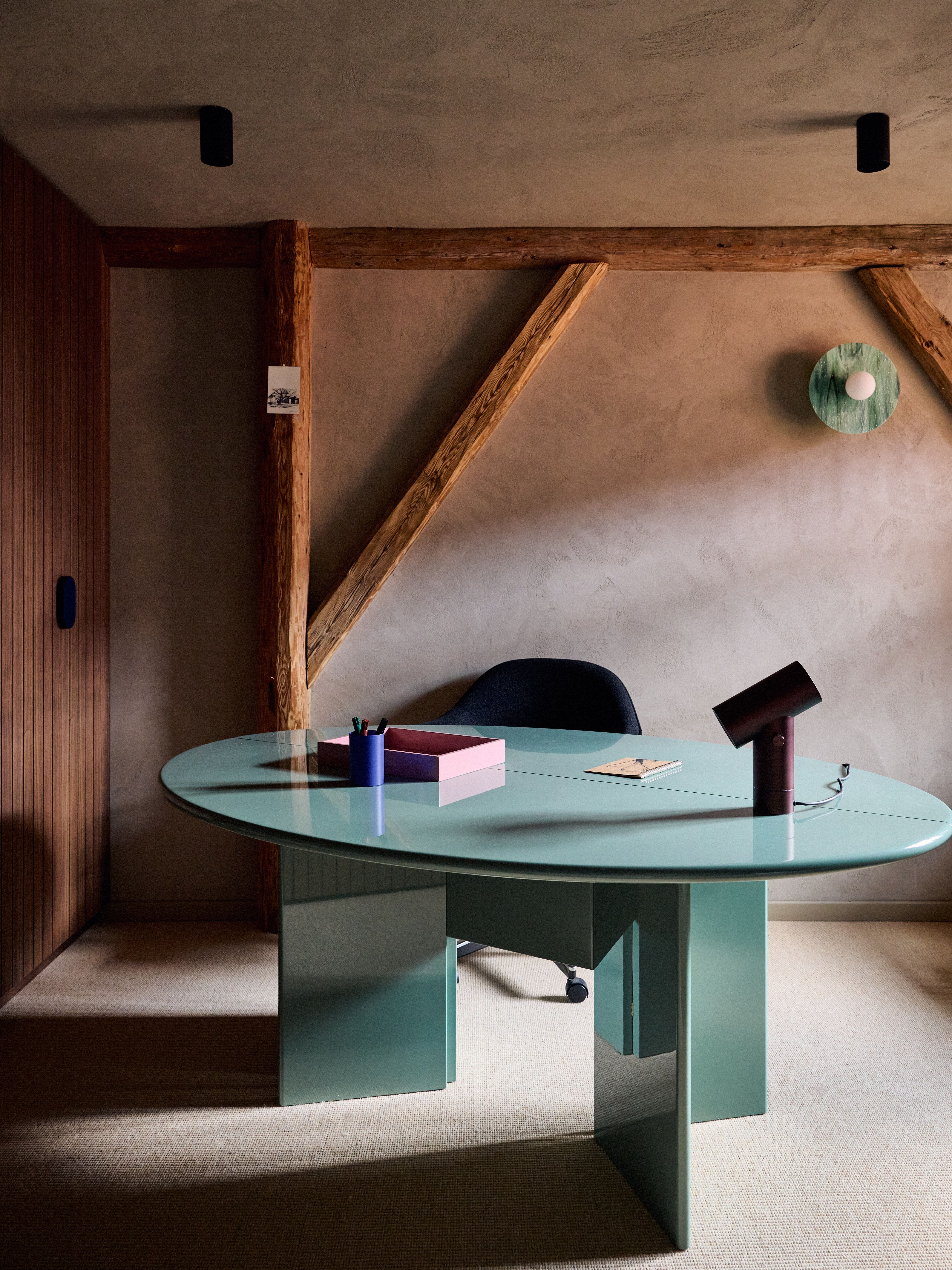 Modernes Home-Office mit skulpturalem, mintfarbenem Design-Schreibtisch vor naturbelassenen Holzbalken und erdigen Wandtexturen.