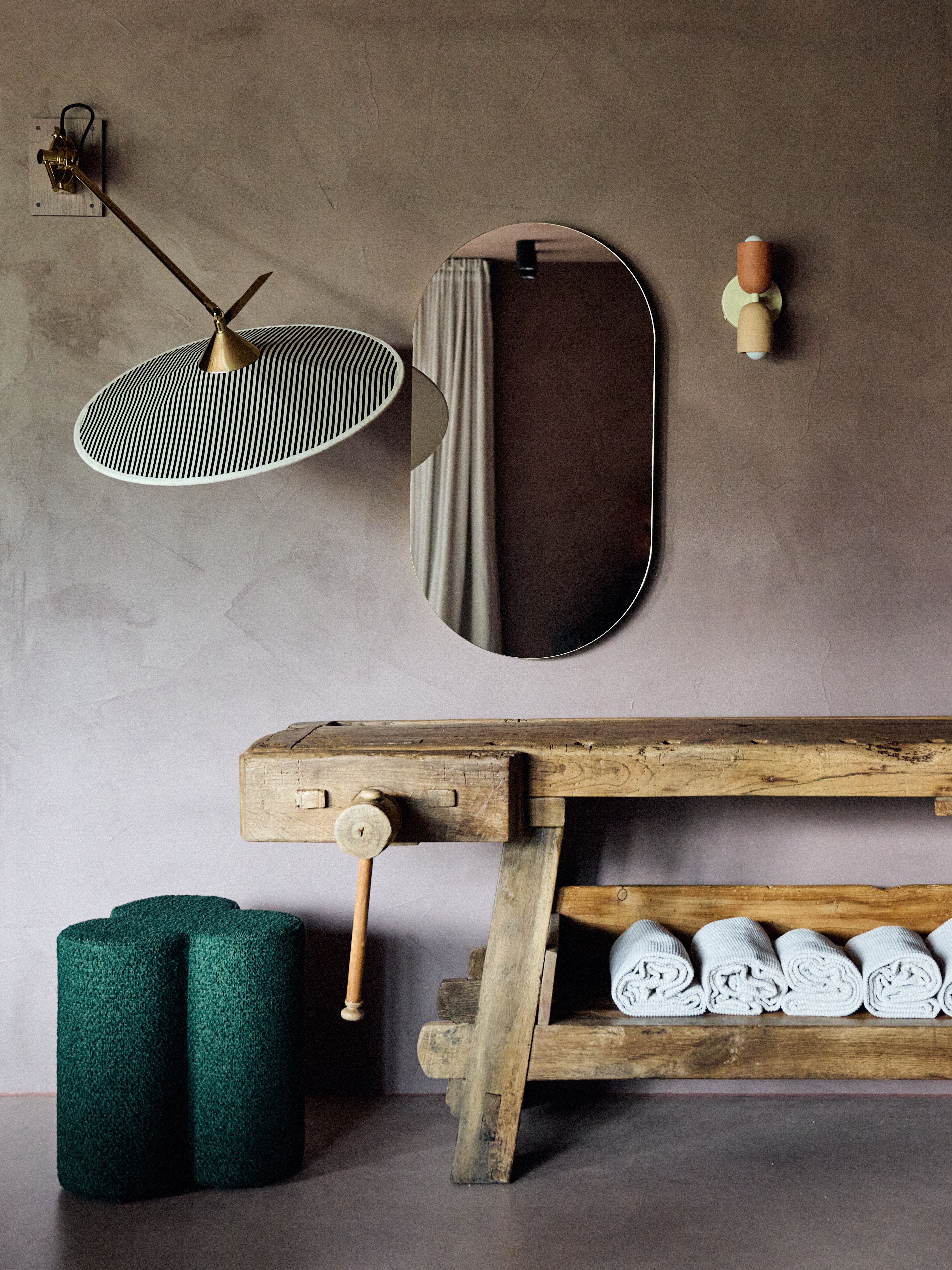 Der Einsatz eines historischen Werkbocks als Konsolenmöbel demonstriert die ästhetische Haltung von Stephanie Thatenhorst, funktionale Spa-Atmosphäre mit texturaler Tiefe und ikonischer Leuchtenpoesie zu verbinden.
