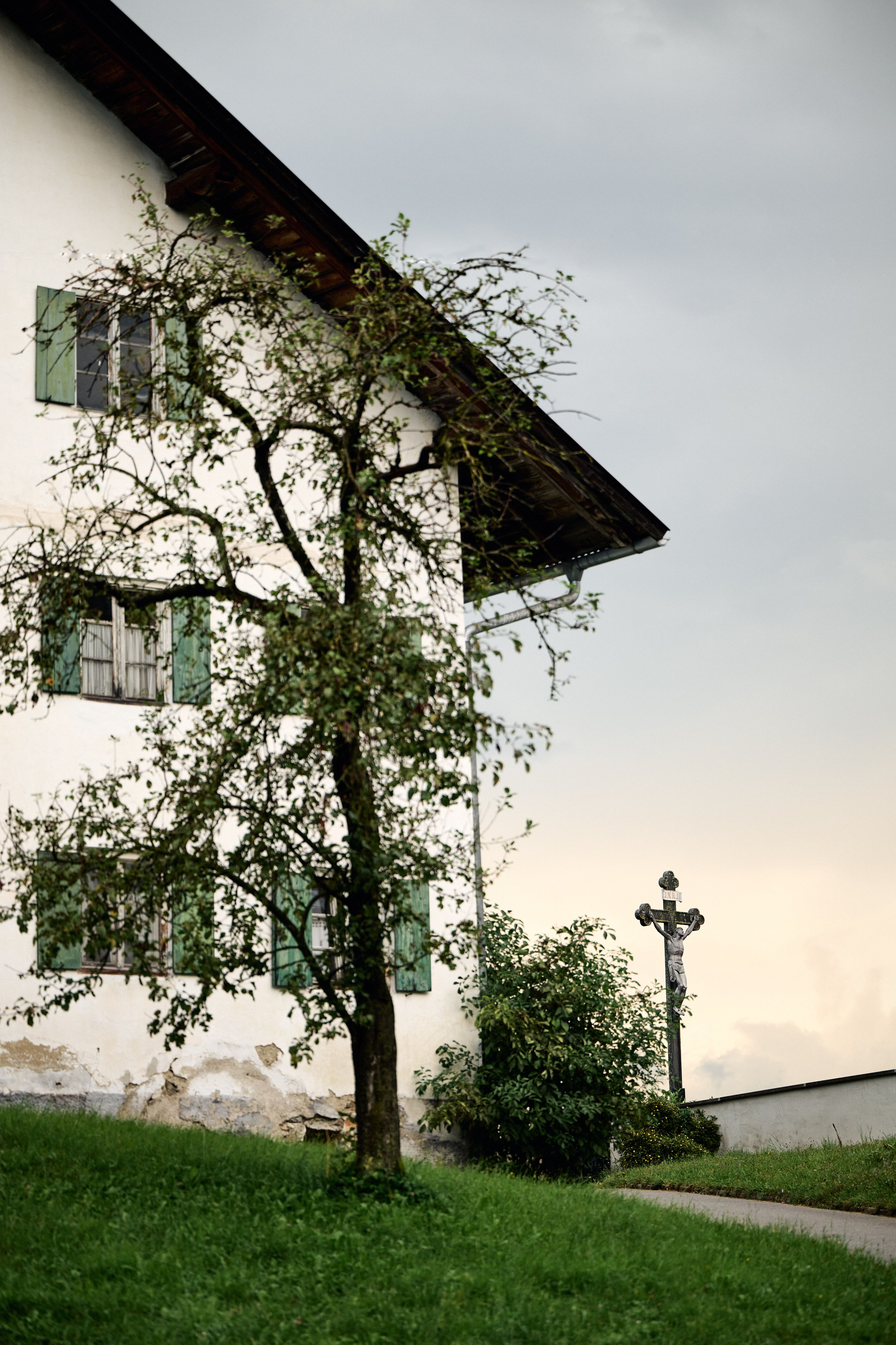 Ein landschaftlich eingebettetes Traditionsensemble, designed by Stephanie Thatenhorst, das gealterte Putzfassade, grüne Läden und stille Dorfpoesie in zeitloser Authentizität vereint.