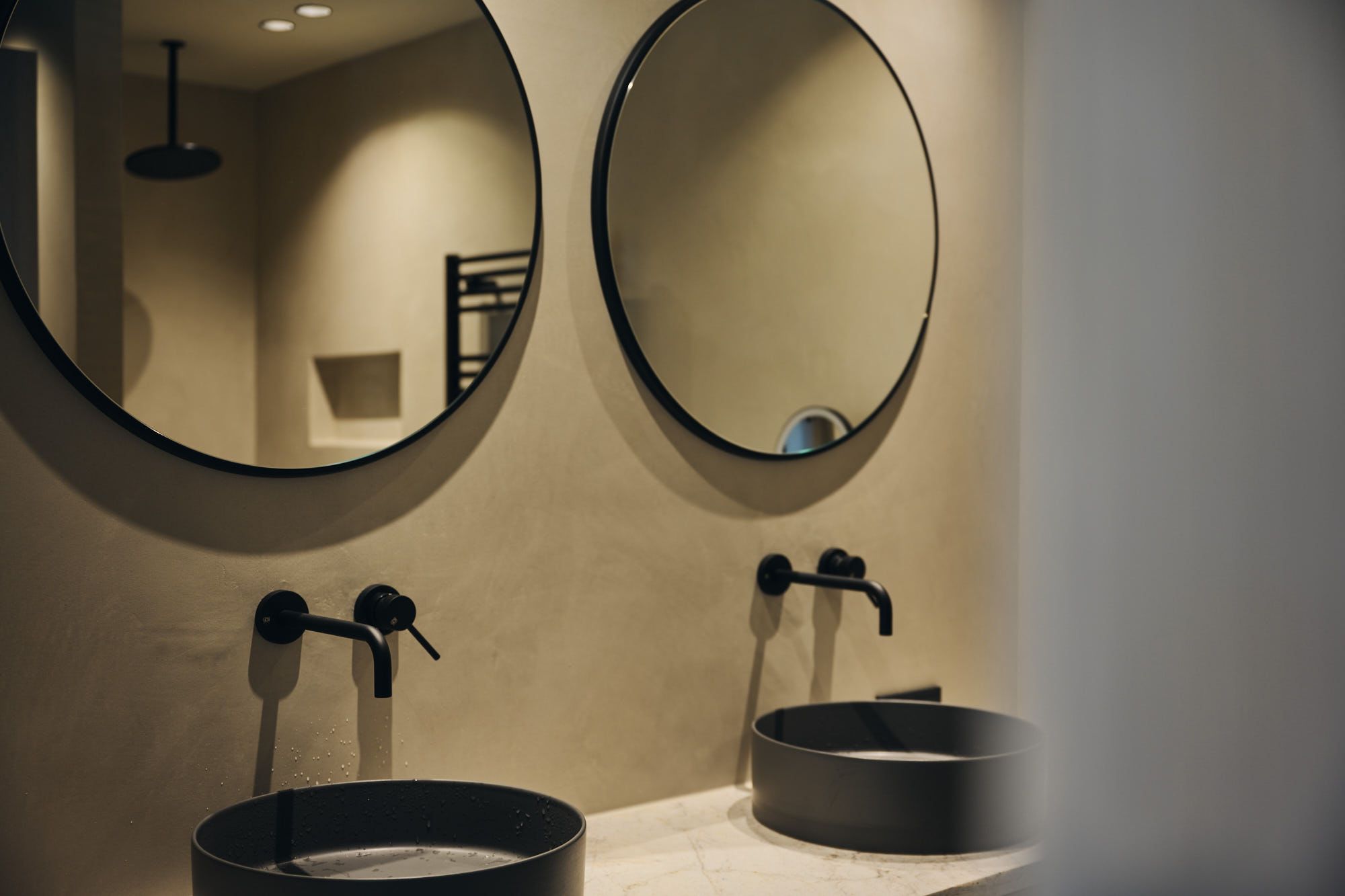 Das puristische Badezimmer im Ullrhaus Hotel, gestaltet von Stephanie Thatenhorst, setzt auf moderne Mineralputzflächen und kontrastierende schwarze Armaturen.