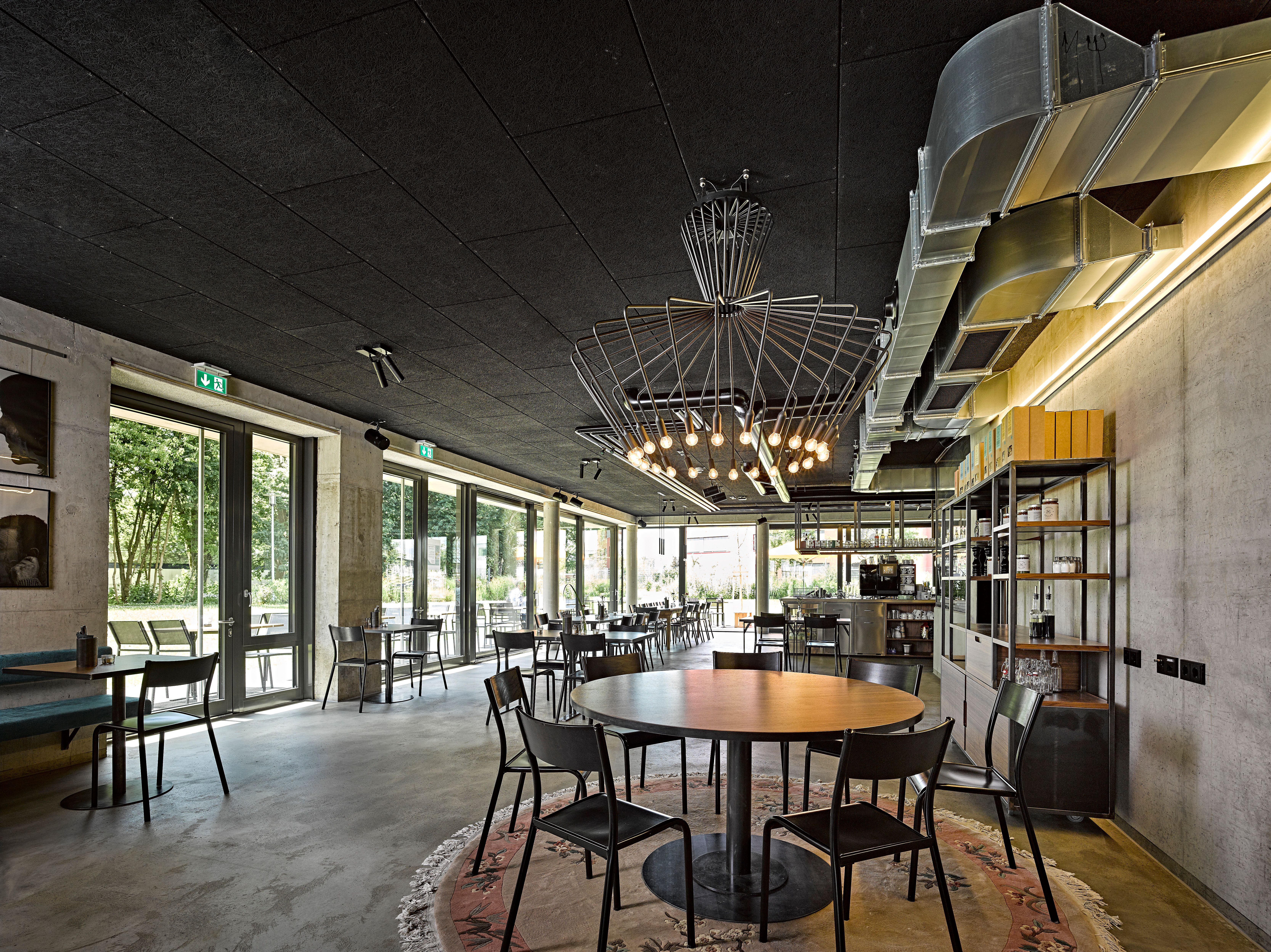 Offener Restaurantbereich in modernem Gastronomiedesign mit hoher Decke, viel Tageslicht und klarer Raumstruktur, entworfen von Stephanie Thatenhorst für Holler Speisen.