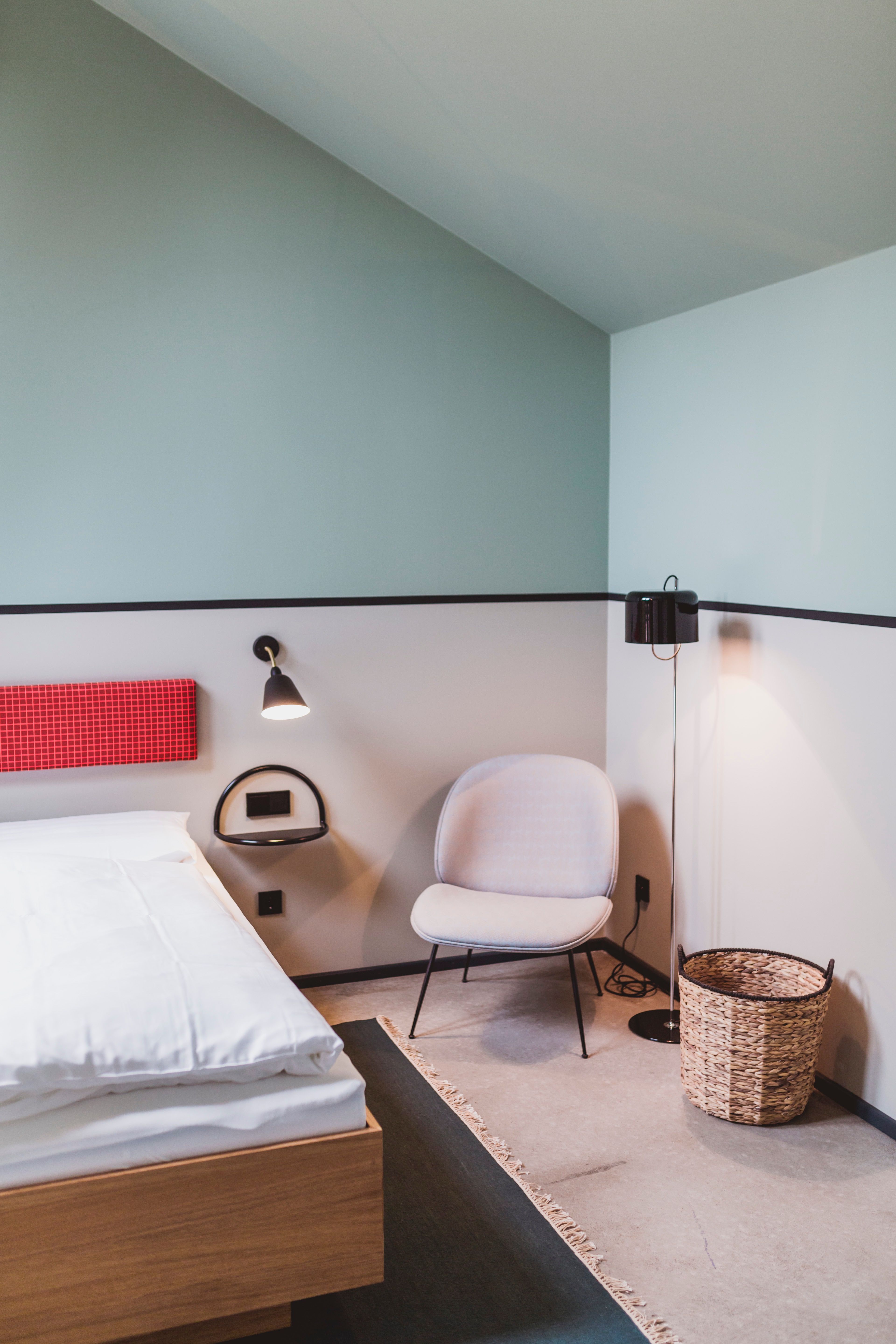 Das Gästezimmer mit Sessel, Leseleuchte und textilen Wandpaneelen zeigt die wohnliche Handschrift des Hotelprojekts Kloster Möllenbeck.