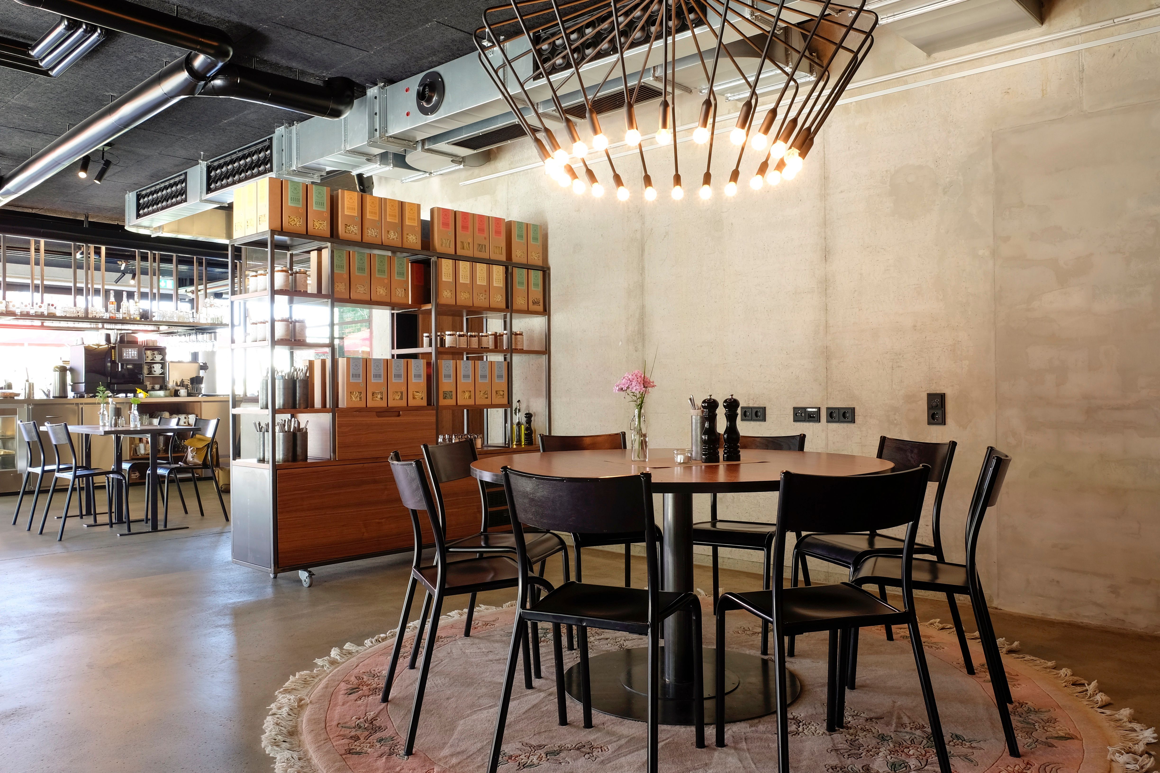 Detailansicht des Essbereichs im Restaurant Holler Speisen, die das Zusammenspiel aus Betonwand, maßgefertigten Möbeln und warmem Lichtkonzept von Stephanie Thatenhorst zeigt.