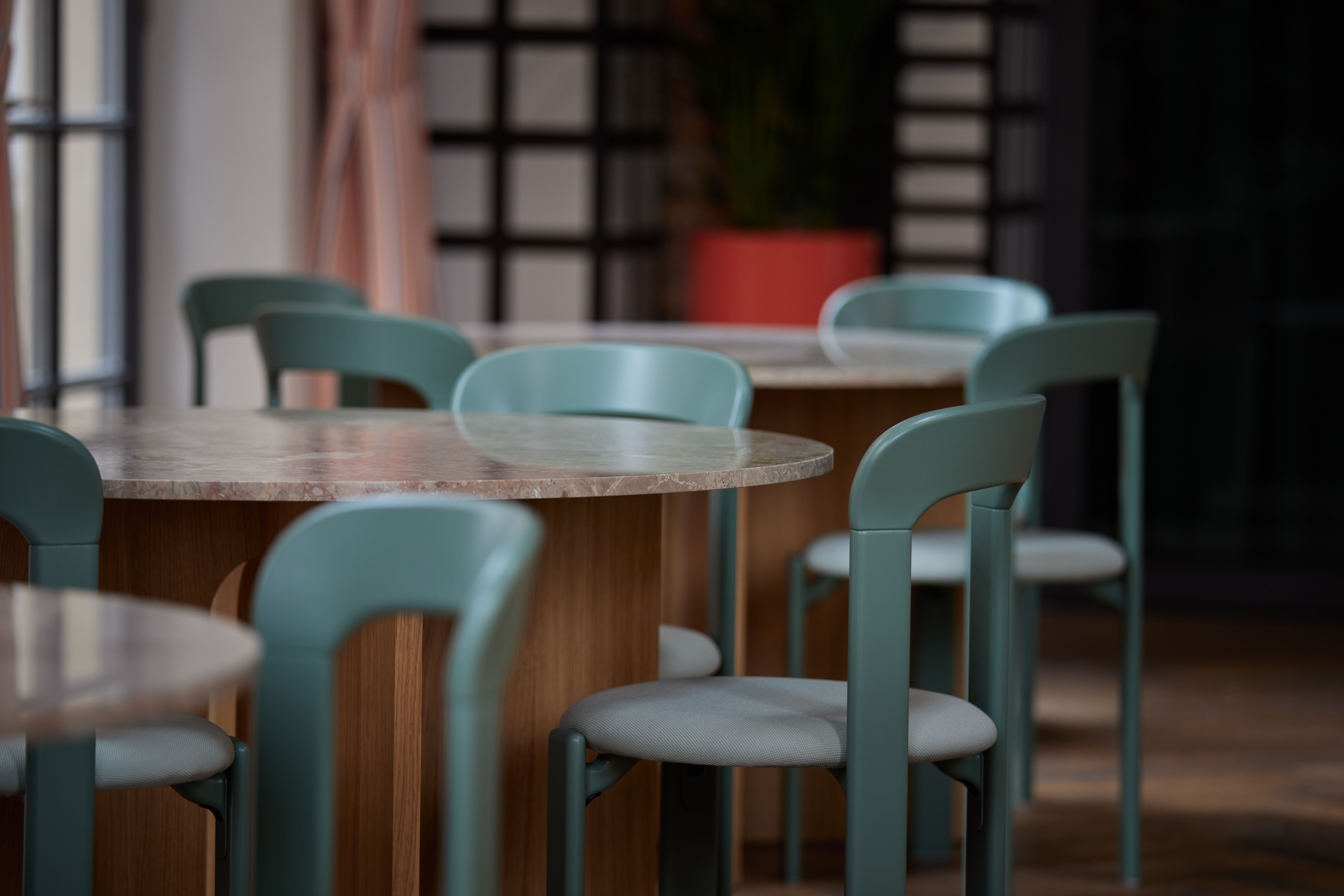 Tonale Restaurantbestuhlung in pastellgrünem Pulverlack-Finish mit Naturstein-Tischplatten, designt von Stephanie Thatenhorst für das Turbinenhaus Kolbermoor – Brasserie.