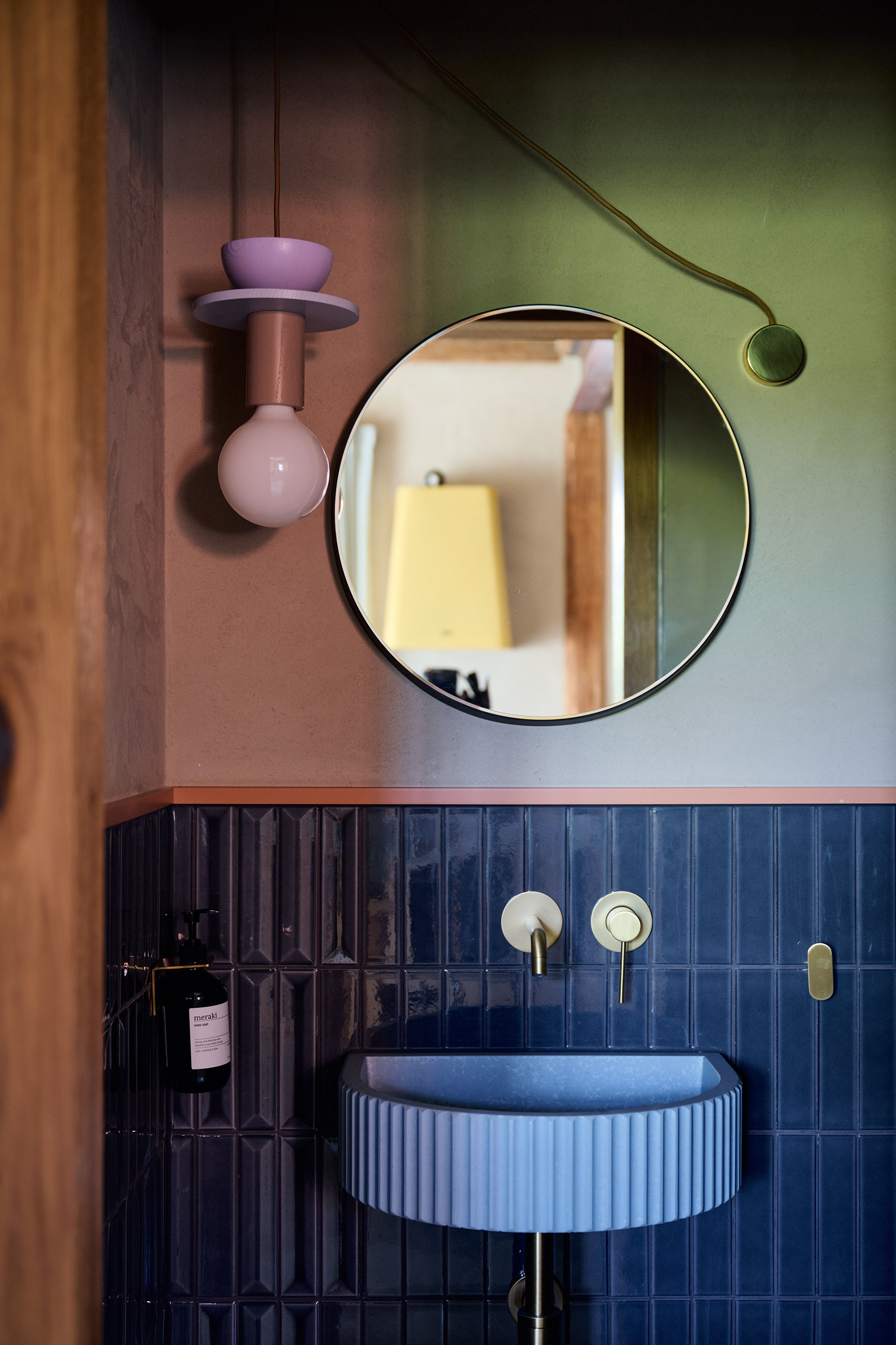 Stilvolles Gästebad mit tiefblauen Strukturfliesen, runden Messingarmaturen und pastellfarbenem Leuchtenobjekt im grafischen Zusammenspiel.