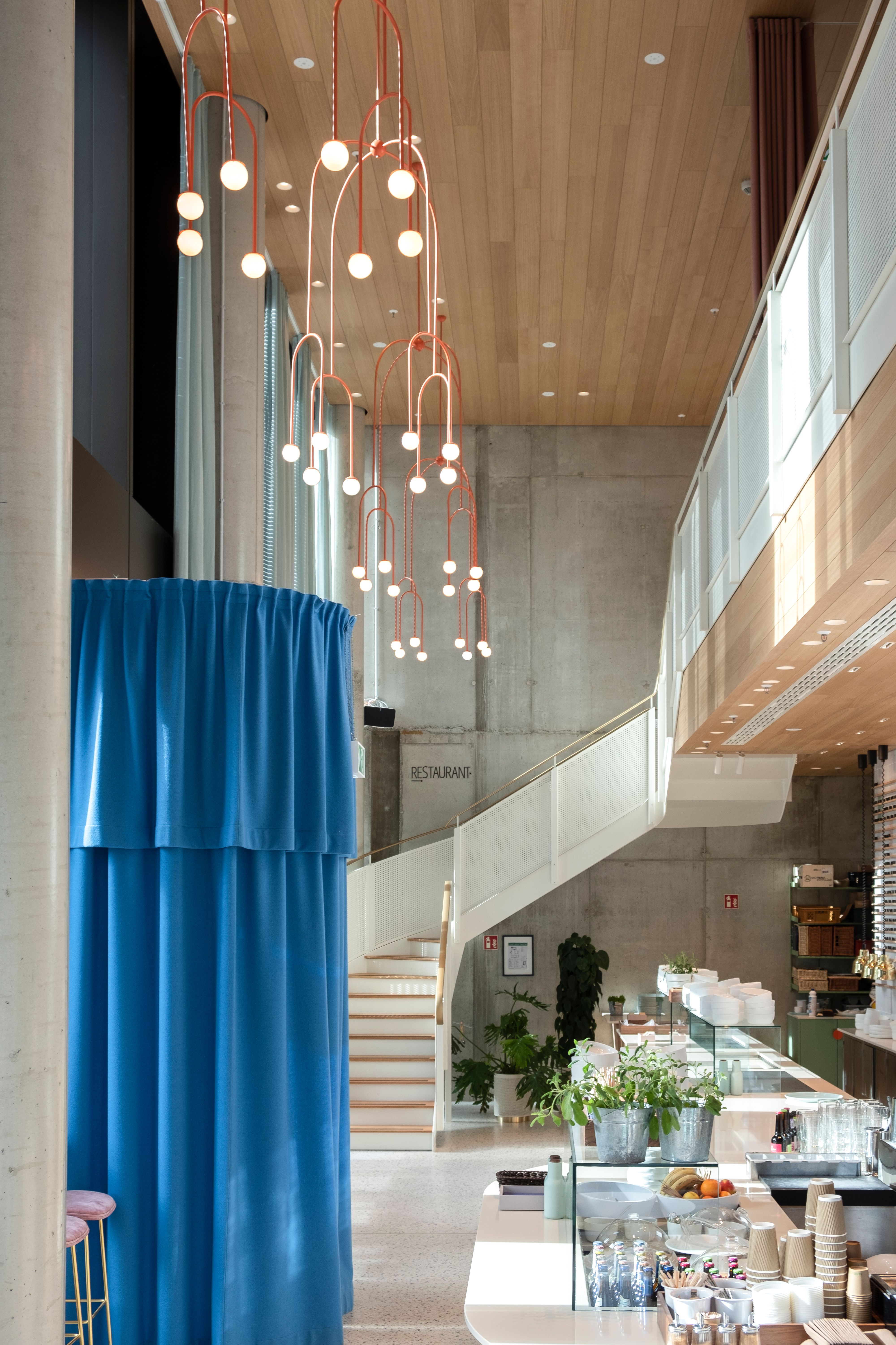 Die hohen Räume des Lilli P, akzentuiert durch skulpturale Pendelleuchten und farbige Vorhänge, zeigen die charakteristische Handschrift von Stephanie Thatenhorst Interior Design.