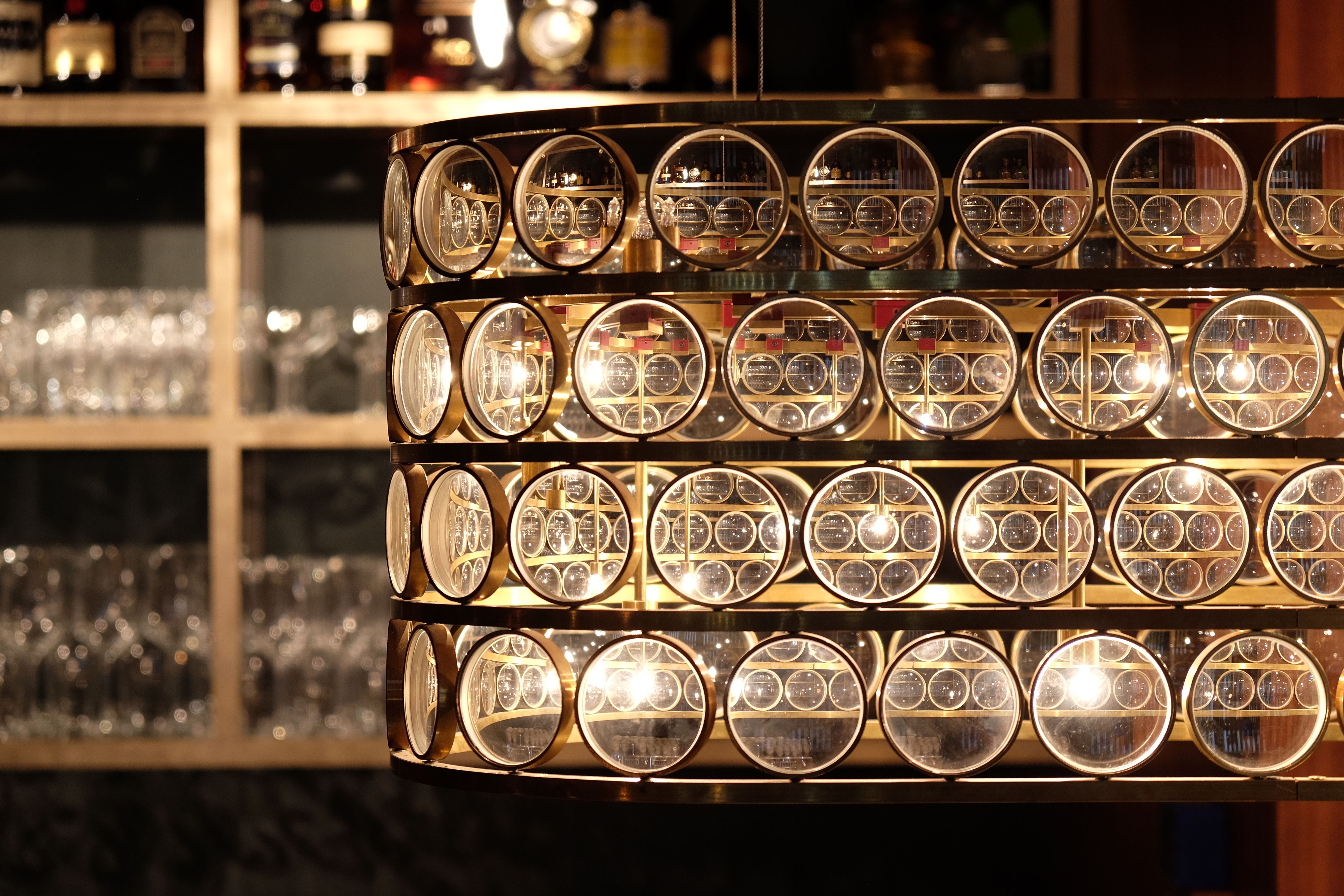 Die detailreiche Barleuchte vor dem Spirituosenregal unterstreicht den hochwertigen Materialmix und die handwerkliche Präzision des Interior Designs.