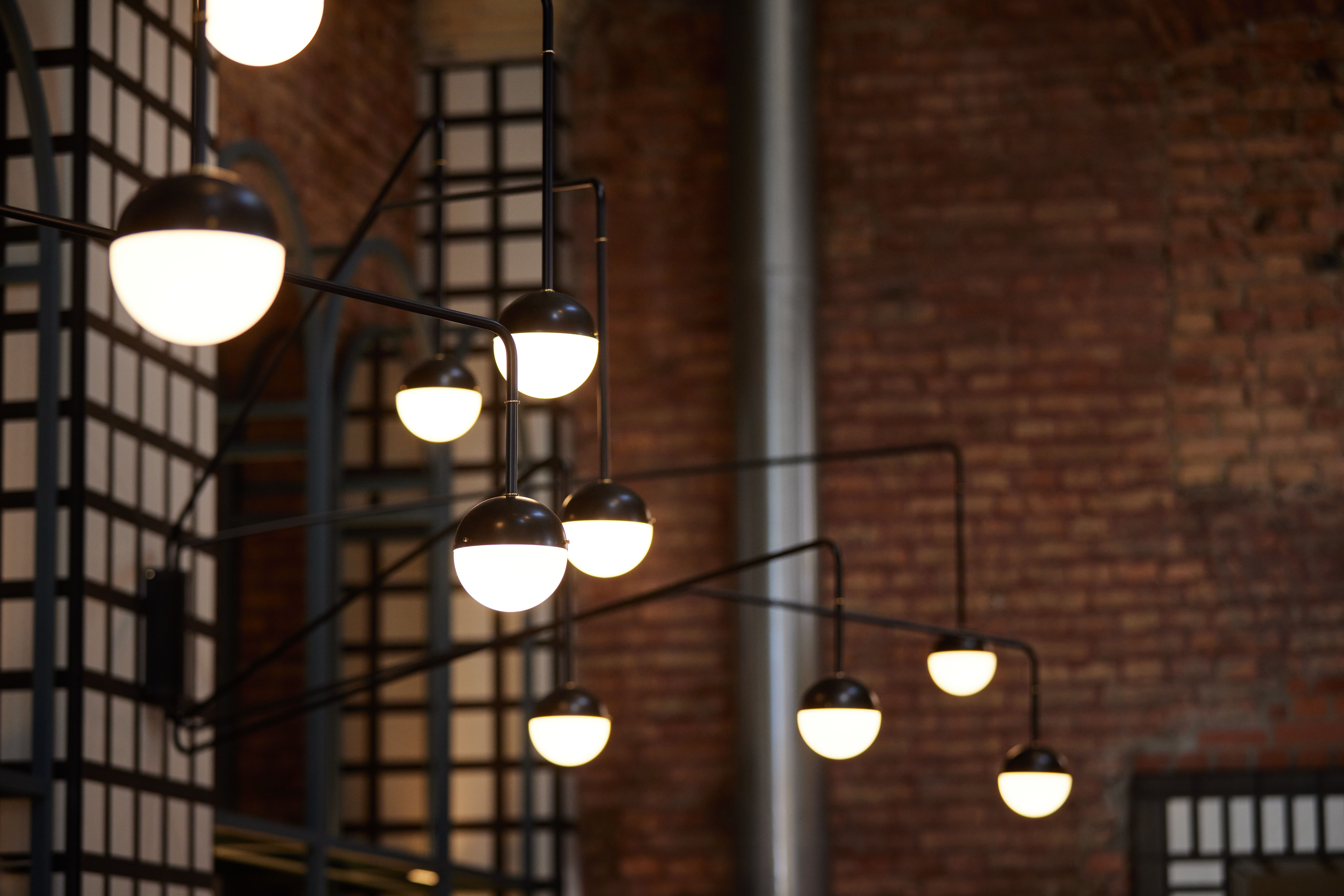 Lichtskulptur im Zylinderkorpus mit Messingapplikation vor freigelegtem Backsteinmauerwerk, designt von Stephanie Thatenhorst für das Turbinenhaus Kolbermoor – Brasserie.