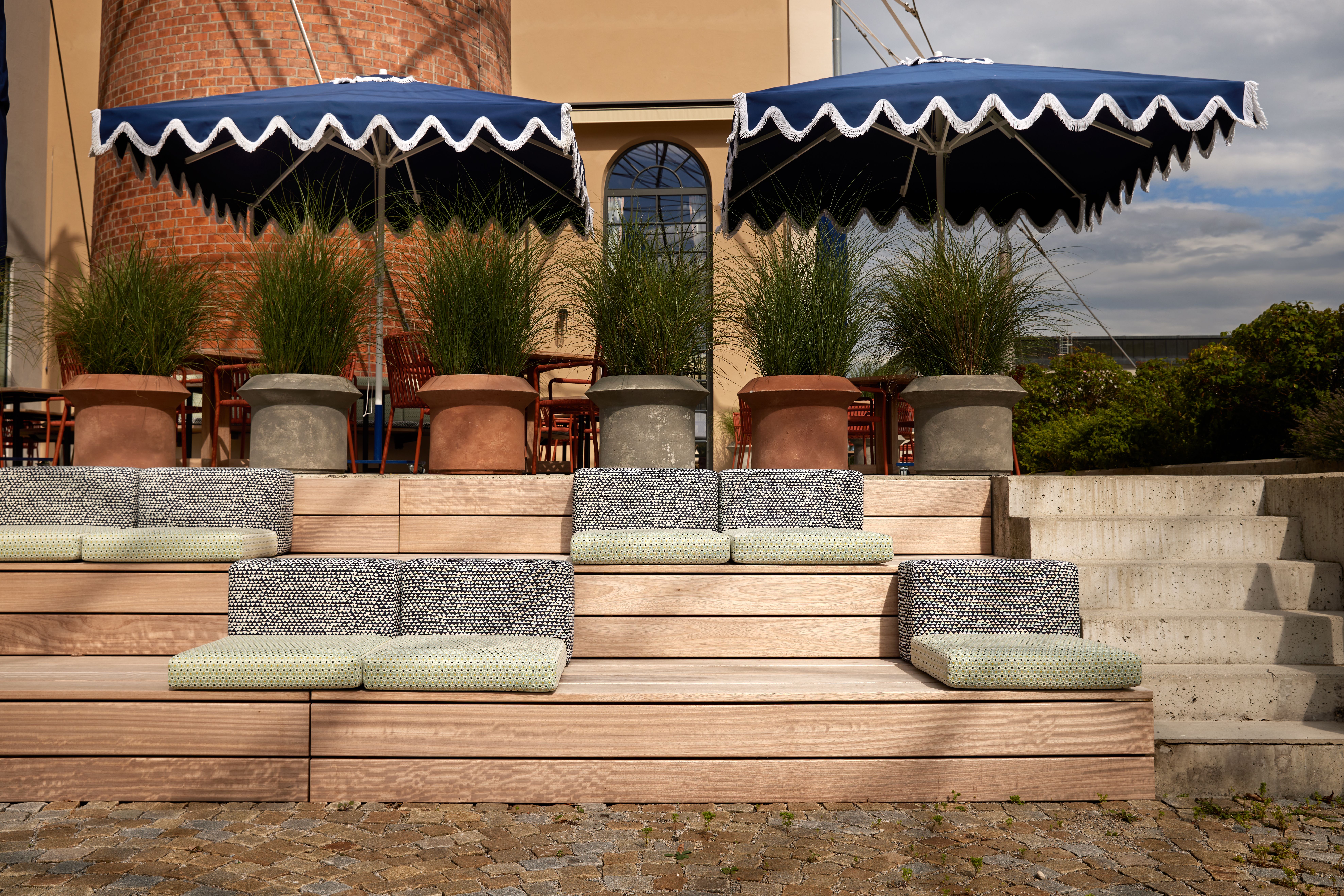 Stufenplateau mit modularer Outdoor-Polsterlandschaft und architektonischer Beetanordnung, entworfen von Stephanie Thatenhorst für das Turbinenhaus Kolbermoor – Brasserie.