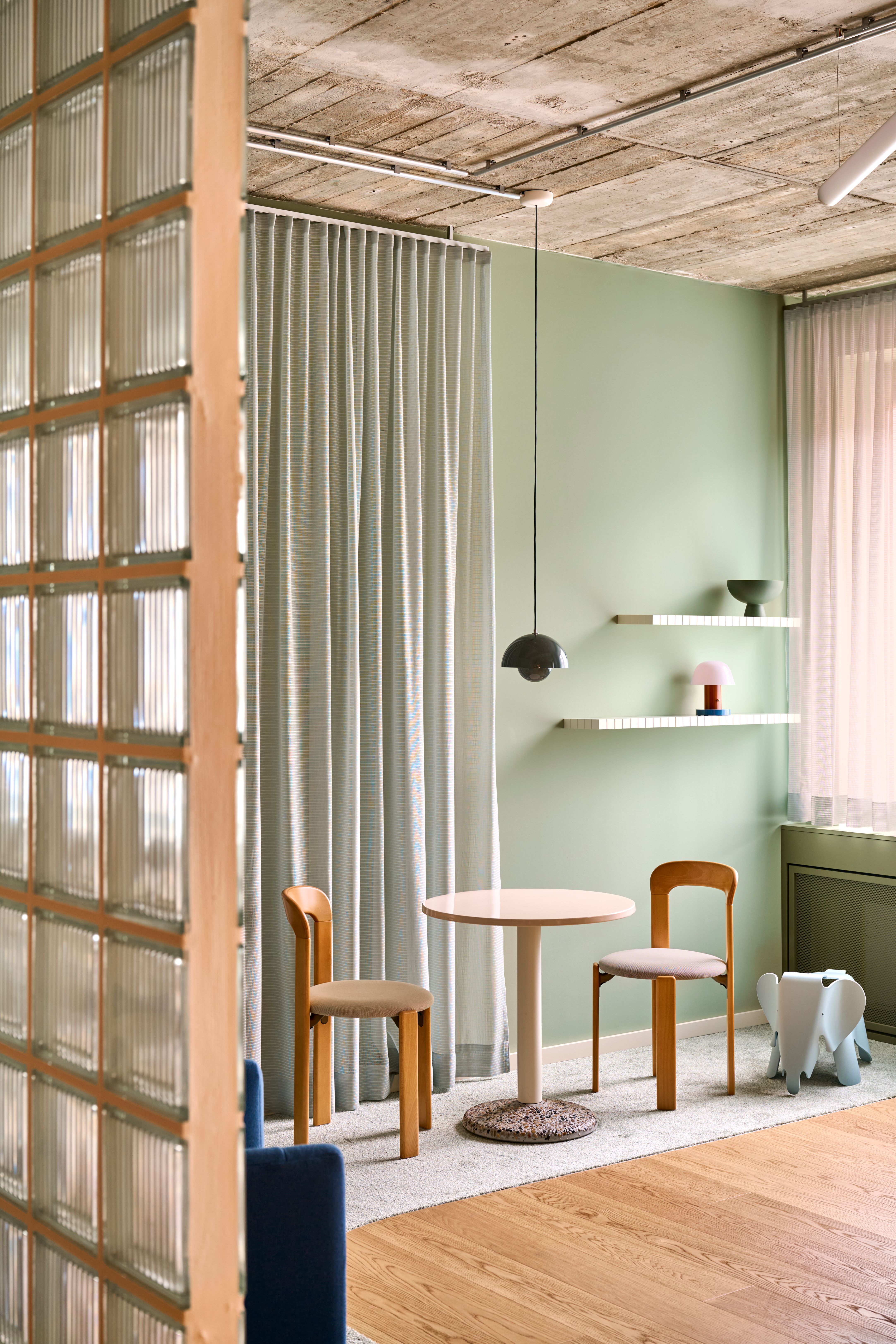 Sanftes Salbeigrün, Designklassiker und dezente Lichtführung schaffen eine freundliche und stilvolle Wartezone im Interior-Konzept von Stephanie Thatenhorst.