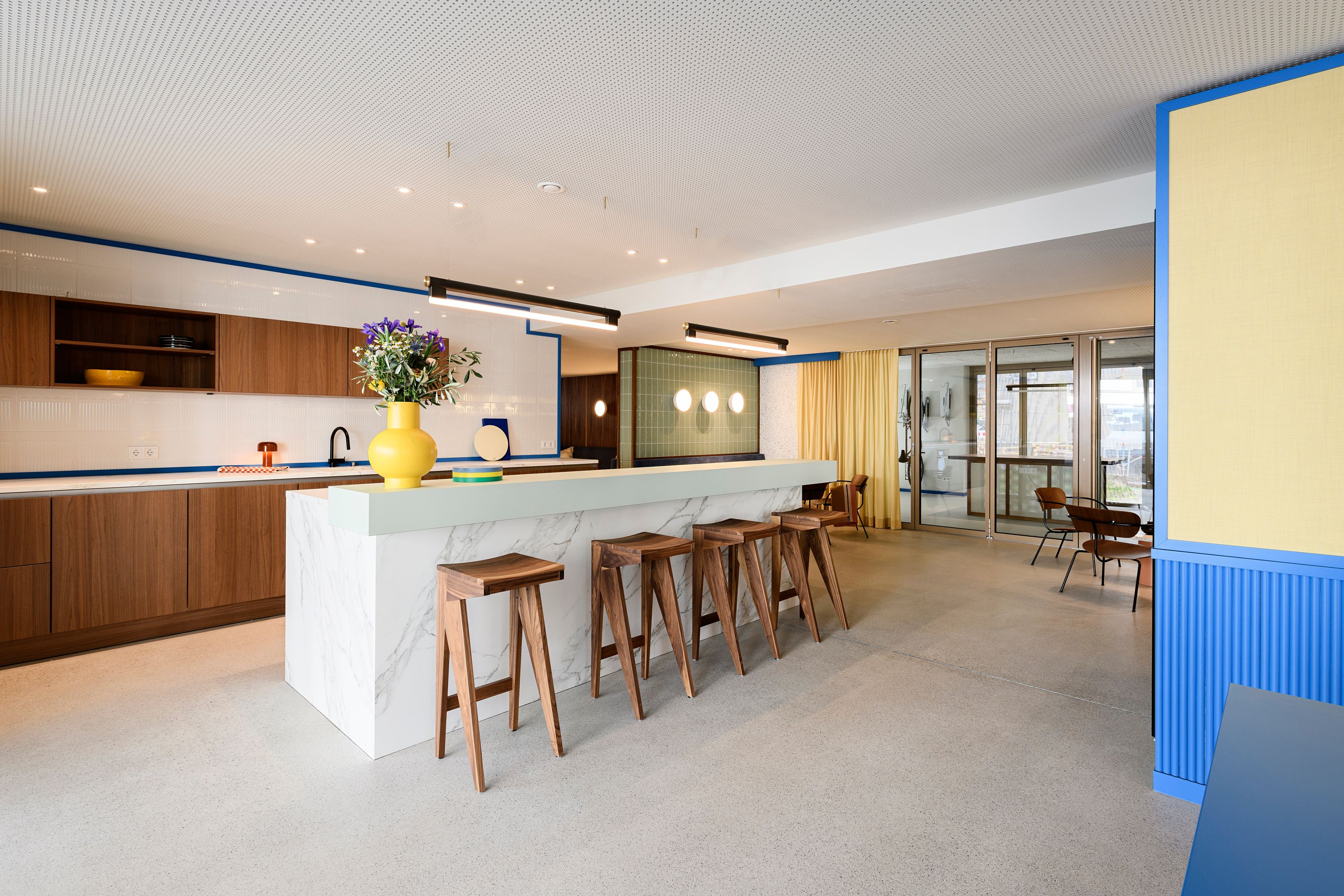Dieses großzügige Küchenensemble mit markanter Marmorinsel und farbigen Akzenten wurde von Stephanie Thatenhorst für die Kupa – Kitchen & Working Lounge designt.