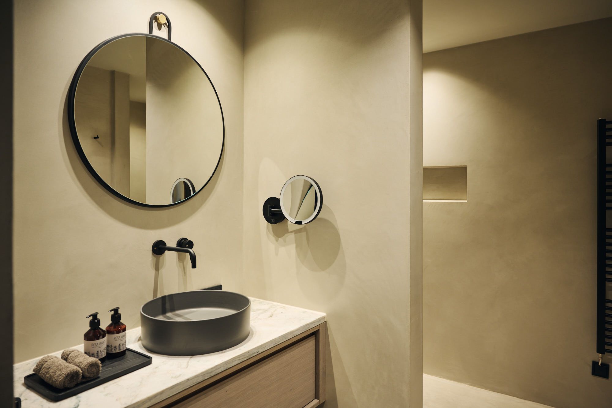 Das Ullrhaus-Badezimmer nach Design von Stephanie Thatenhorst präsentiert sich mit puristischen Formen, einem runden Spiegel und edlen Naturtönen.