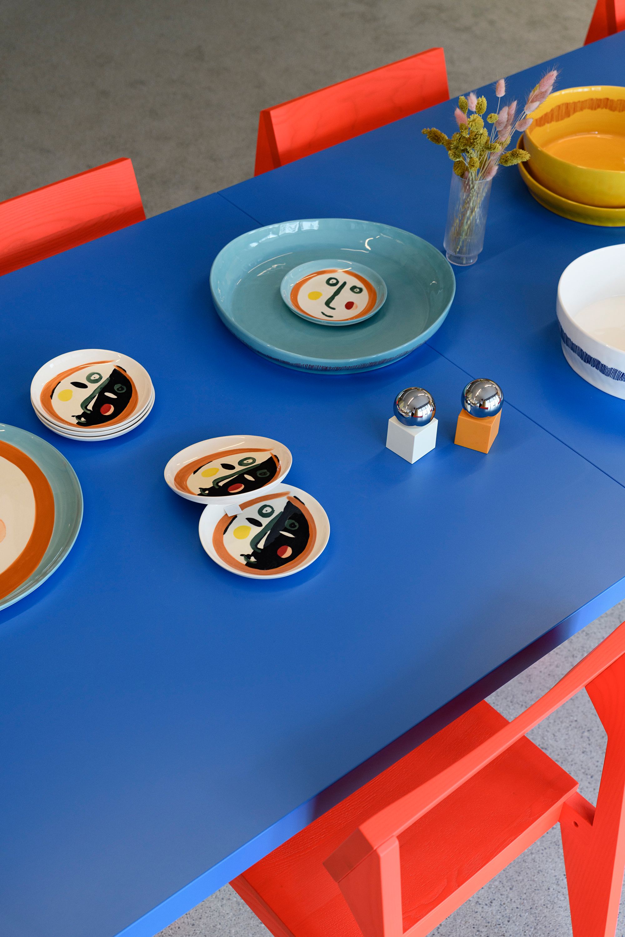 Die farbenfrohe Tischkultur in der Kupa – Kitchen & Working Lounge, gestaltet von Stephanie Thatenhorst, verbindet künstlerische Keramik mit kräftigen Akzenten in Blau, Orange und Gelb zu einem lebendigen Interior-Statement.