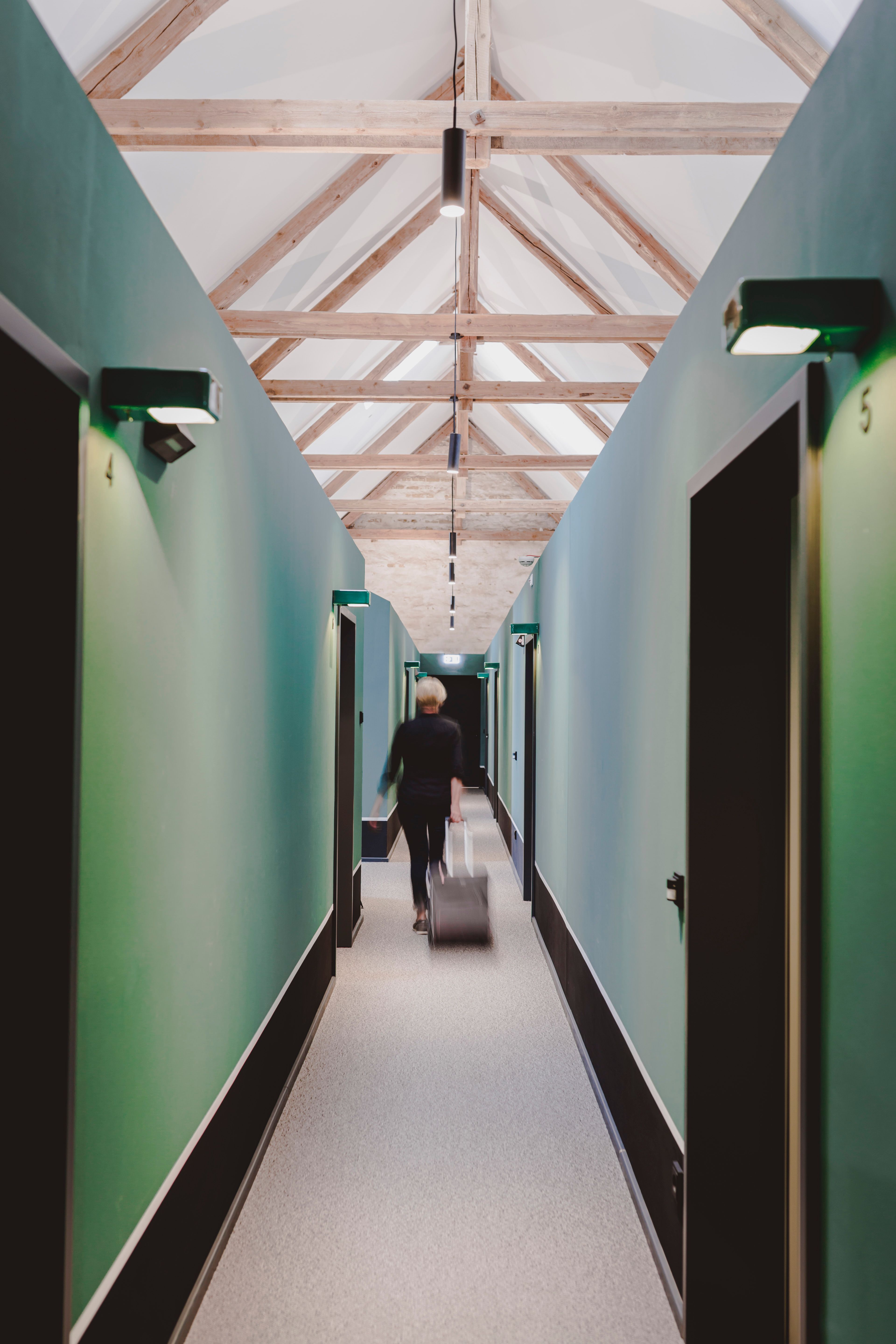 Der lange Hotelflur mit grünen Wänden, Dachkonstruktion und klarer Wegeführung ist ein prägendes Raumelement des Hotelprojekts Kloster Möllenbeck.