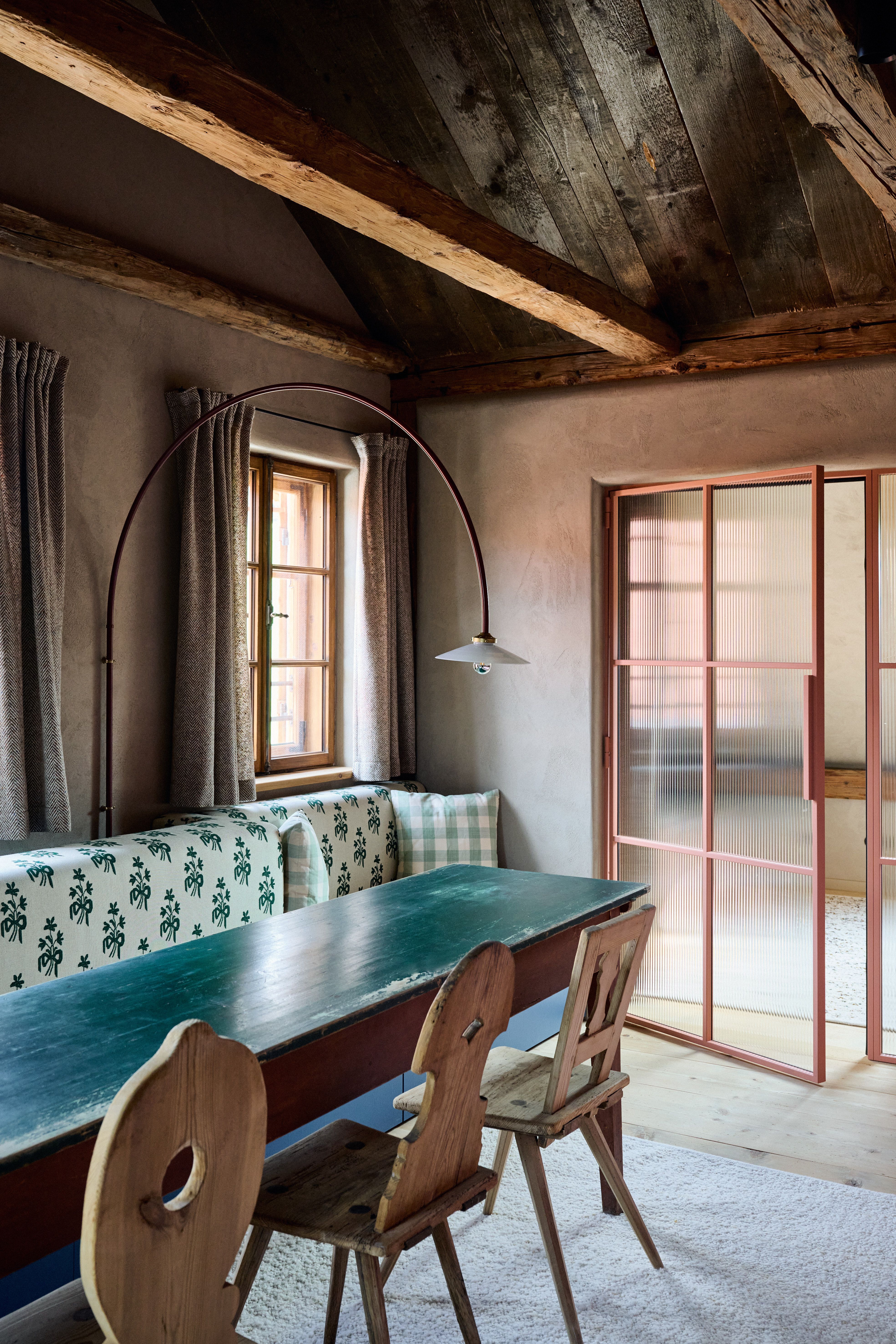 Traditionelle Stubensitzbank mit grün bedrucktem Polsterstoff, historischen Holzstühlen und roségerahmter Schiebetür aus strukturiertem Glas.
