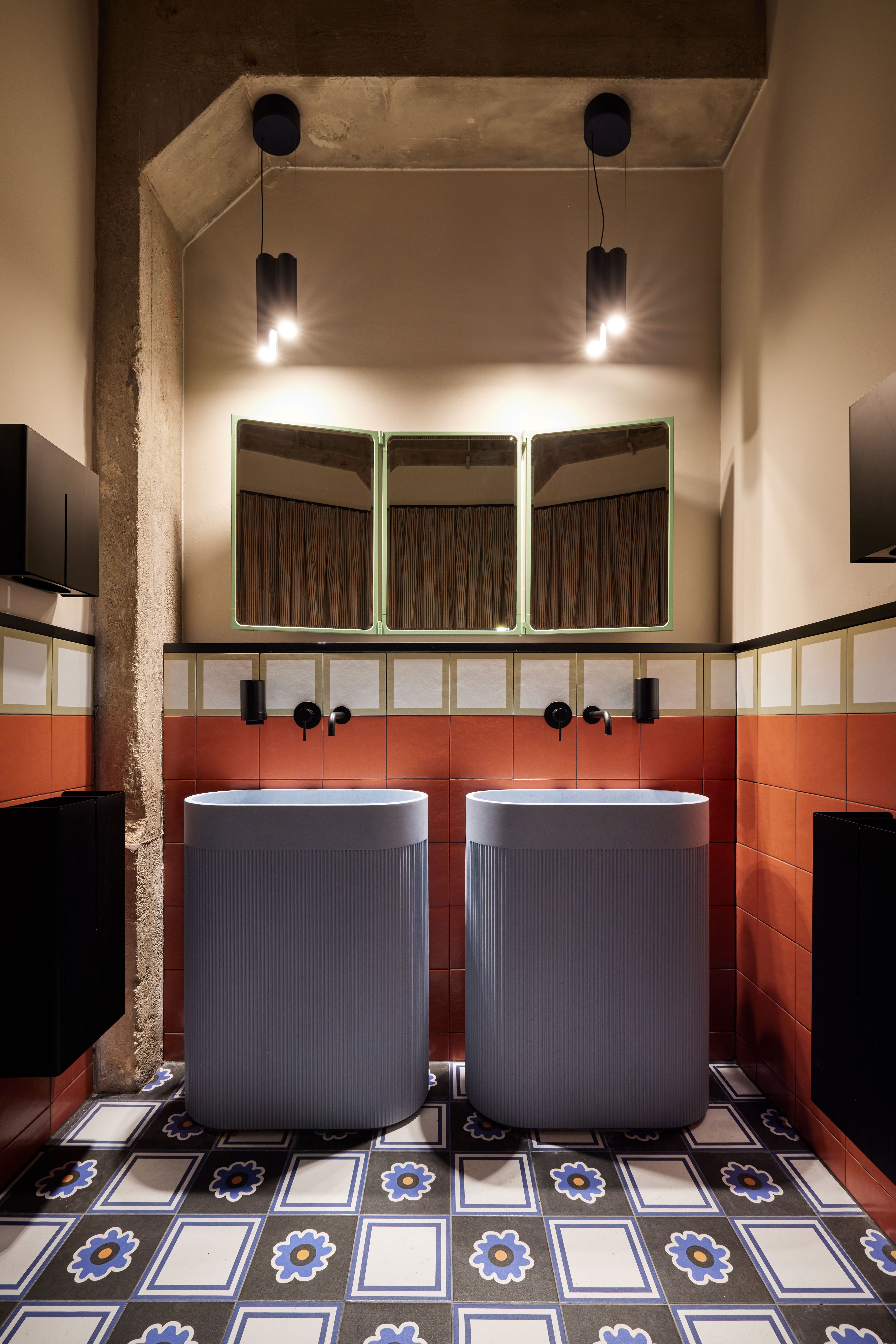 Die freistehenden Waschsäulen mit vertikaler Riffelstruktur, mattschwarzer Armaturik und rahmenloser Triptychon-Spiegelfront wurden im Turbinenhaus Kolbermoor – Brasserie von Stephanie Thatenhorst designt.