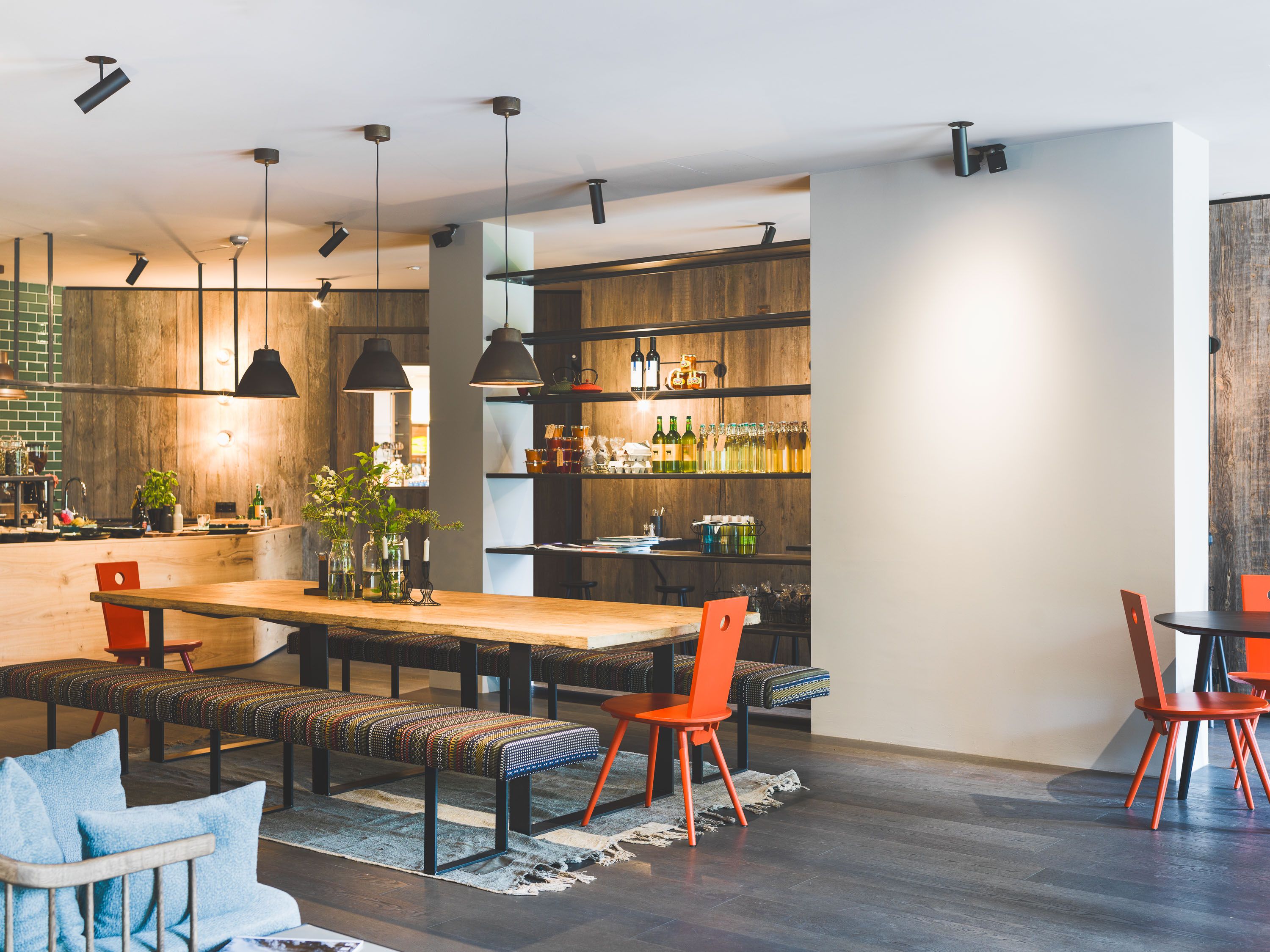 Der großzügige Gemeinschaftsraum des Schönherrhaus Hotels kombiniert lange Holztische, offene Regale und moderne Leuchten zu einem kommunikativen Raumkonzept.