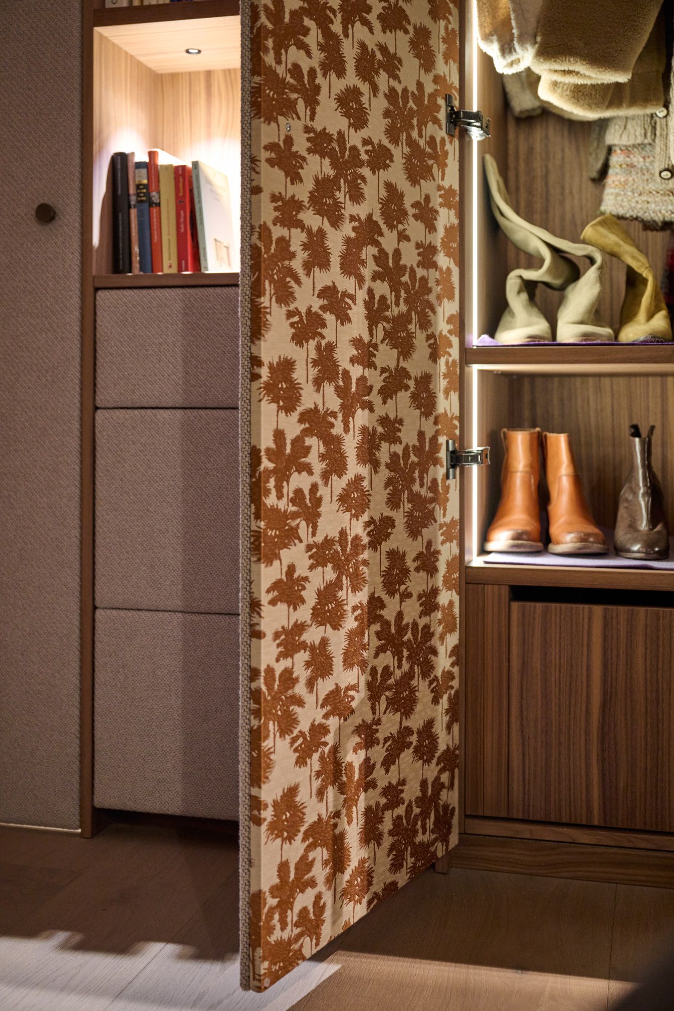 Eleganter Stauraumbereich mit stoffbezogenen Fronten, floraler Textur und warm beleuchteten Holzregalen für ein stilvoll organisches Wohnambiente.