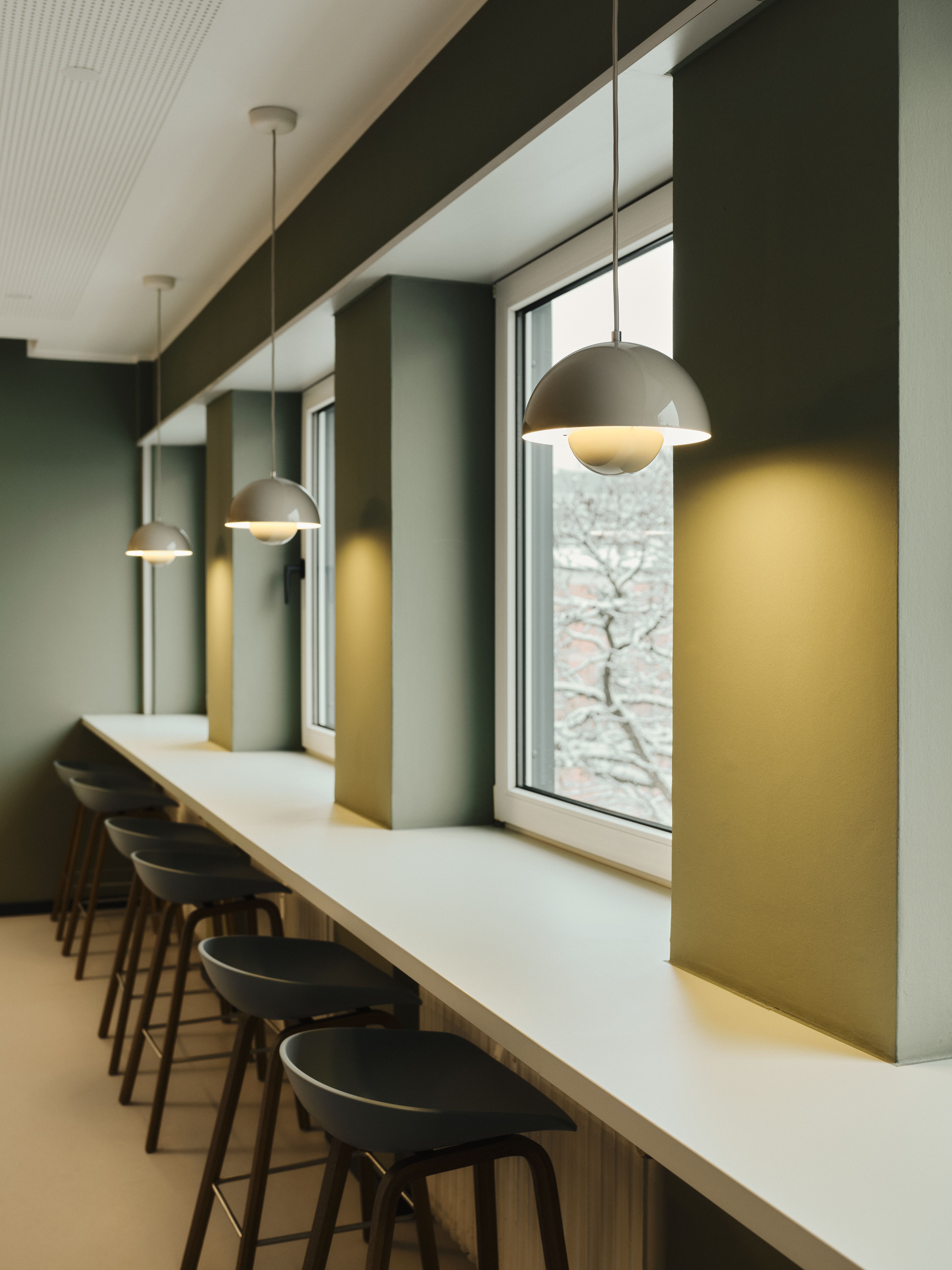 Die barähnliche Fensterzone kombiniert minimalistische Beleuchtung und funktionale Sitzplätze mit ruhigen Grüntönen, designed by Stephanie Thatenhorst.