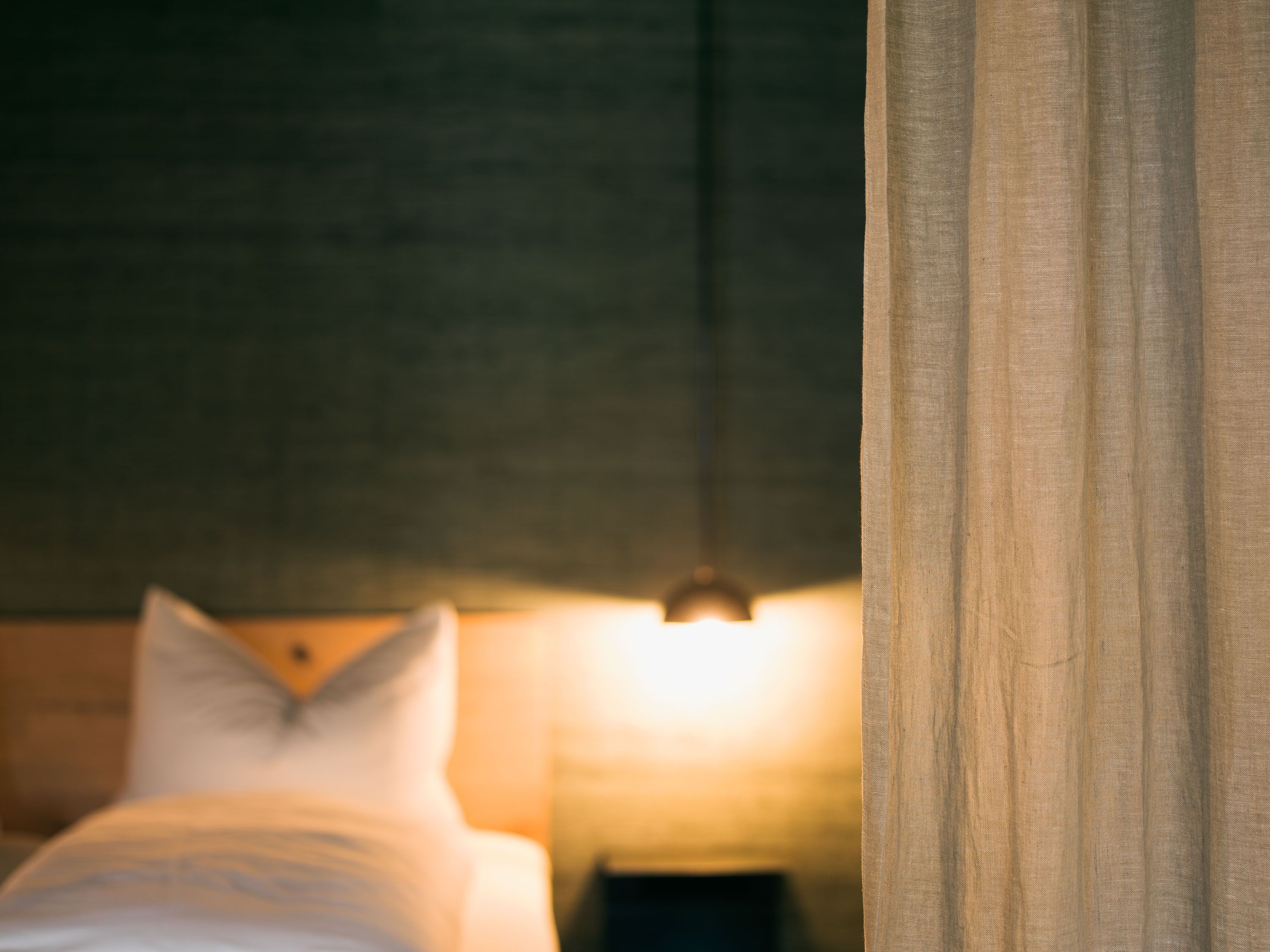 Das Bad im Schönherrhaus Hotel setzt mit Natursteinwaschbecken, Holzablagen und dezenten Fliesen auf zeitlose Eleganz und hochwertige Materialien.