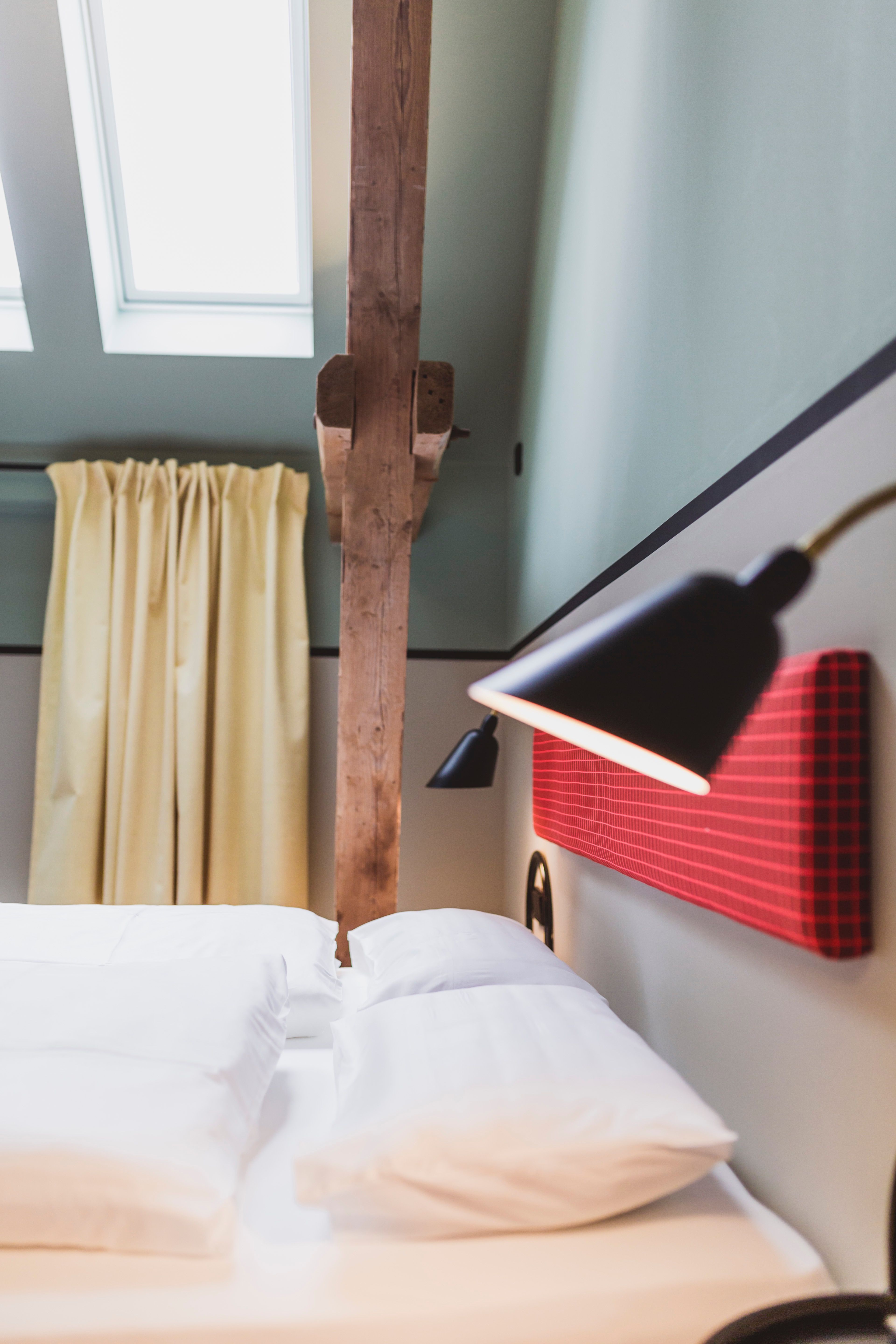 Das Bett mit farbigem Kopfteil, Holzdetails und Dachfenstern ist Teil des ganzheitlichen Interior Designs von Stephanie Thatenhorst im Kloster Möllenbeck.