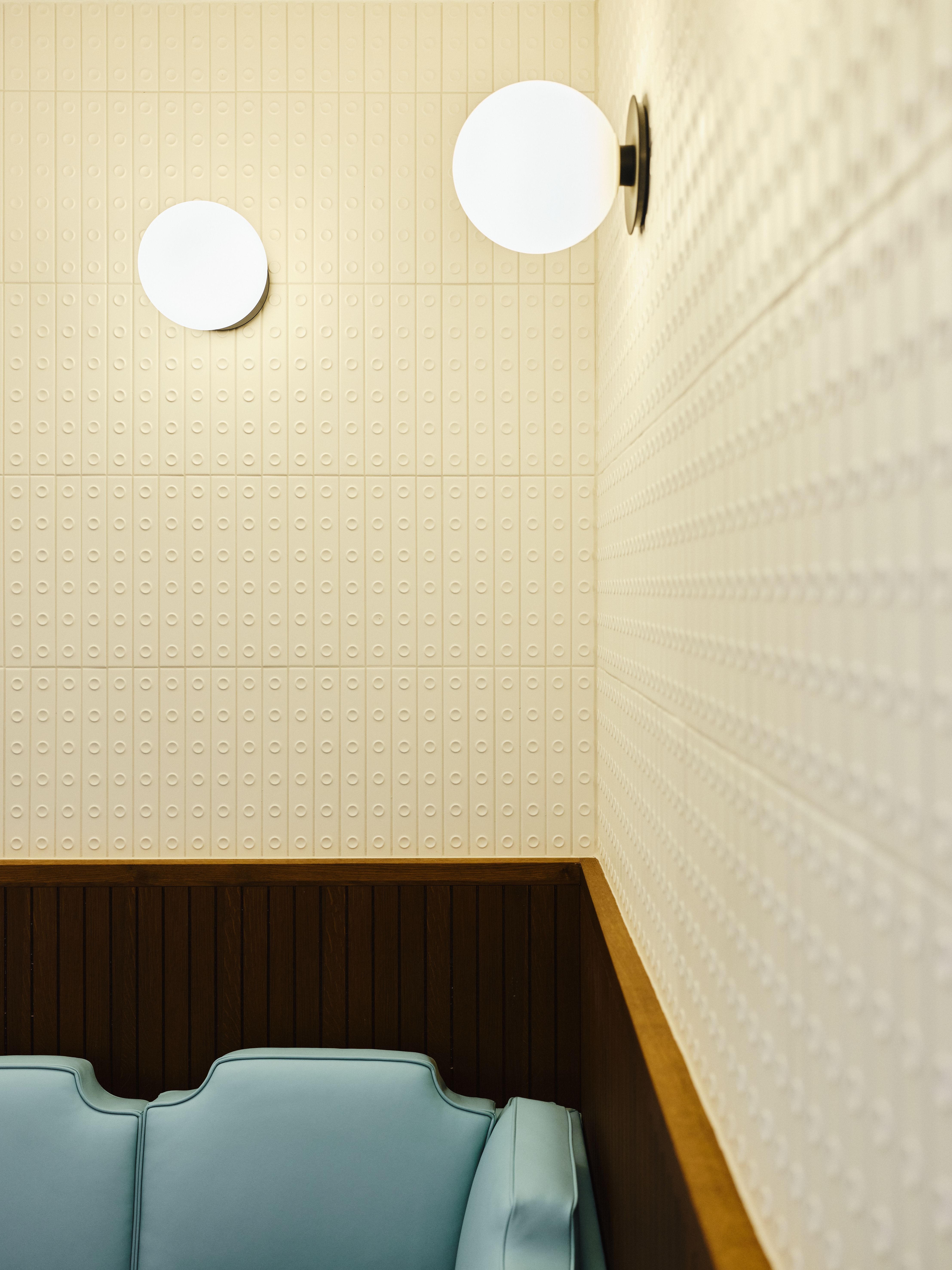 Strukturiert reliefierte Wandfliesen und runde Leuchten schaffen ein ruhiges, hochwertiges Ambiente im Sitzbereich, designed by Stephanie Thatenhorst.