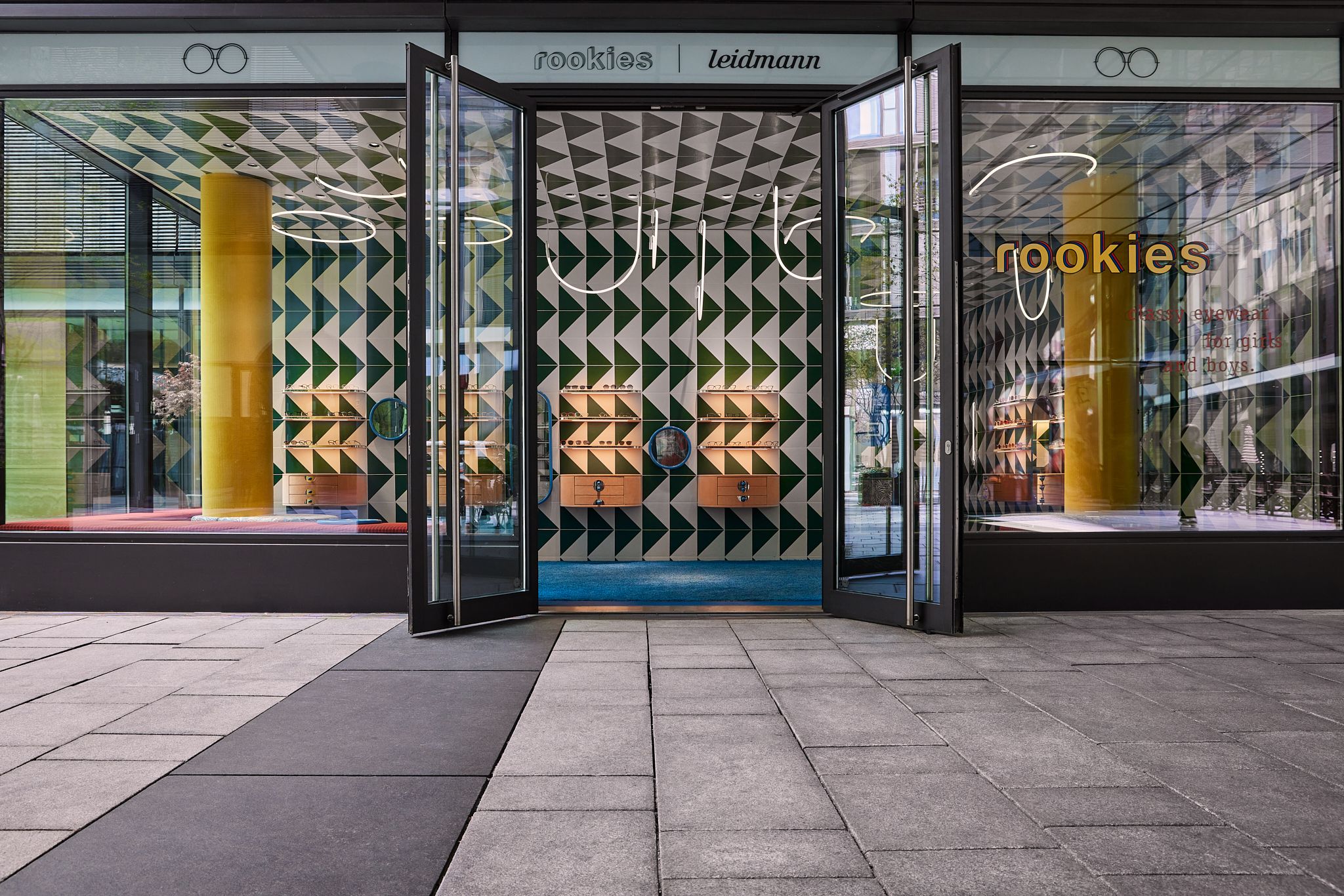 Die Außenansicht mit geöffnetem Eingangsbereich inszeniert die markante Gestaltungssprache, die Stephanie Thatenhorst für den Store Rookies – Eyewear for Kids geschaffen hat.