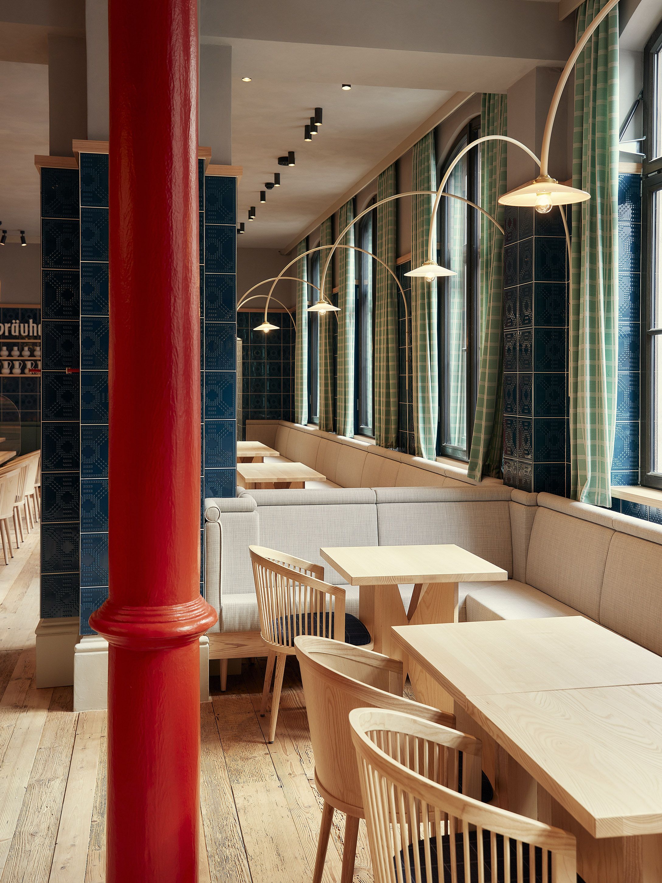 Der langgestreckte Gastraum kombiniert helle Holztöne, blau glasierte Kacheln und weiche Textilien zu einer zeitgenössischen Wirtshausatmosphäre, gestaltet von Stephanie Thatenhorst.