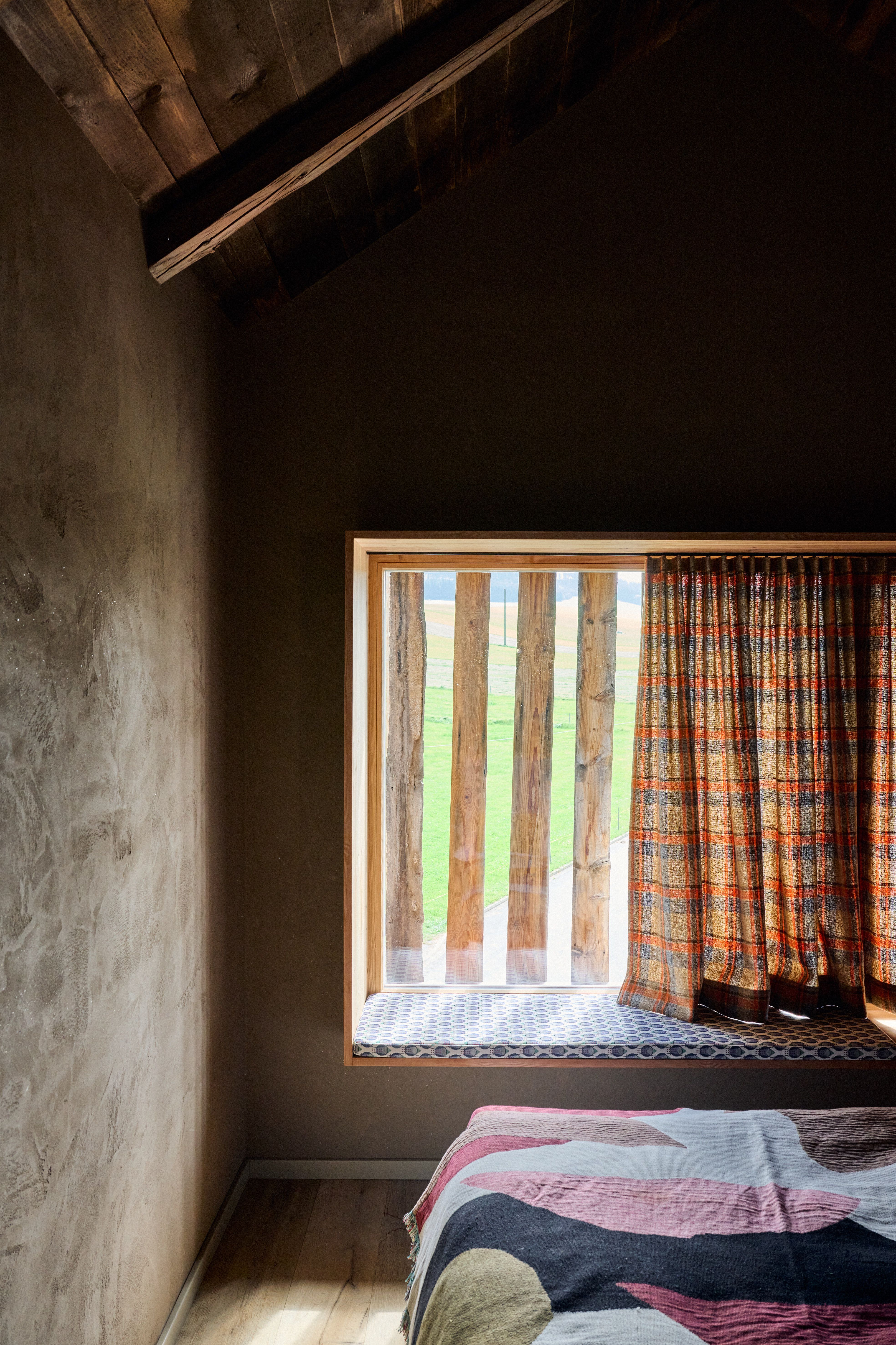 Reduzierter Schlafbereich mit rustikaler Holzdecke, textiler Fensterbank und halbtransparenter Landhausgardine als moderne Alpeninterpretation.