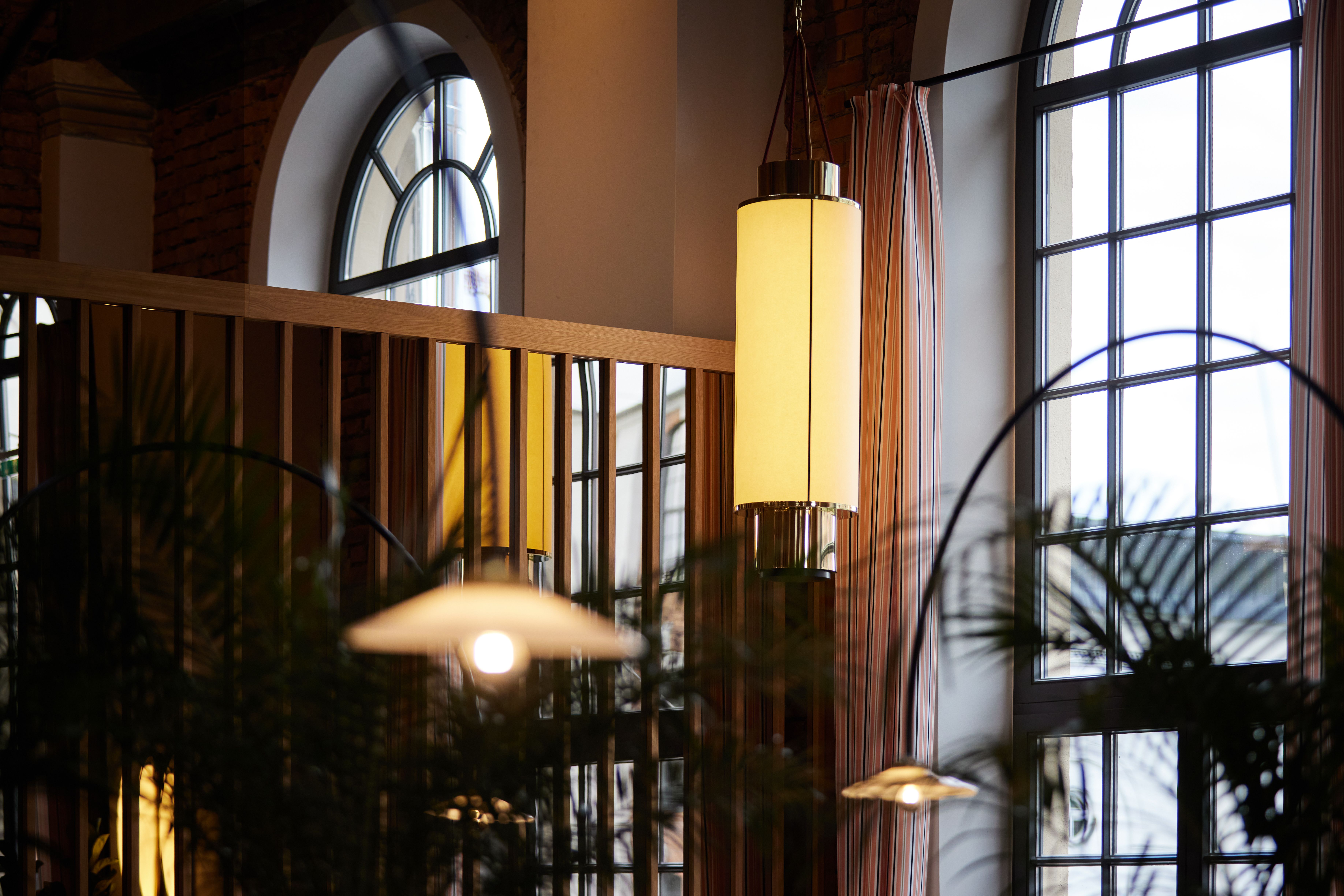 Großformatige Pendelleuchte im historischen Fensterachsenraster mit architektonischer Raumhöhe, gestaltet von Stephanie Thatenhorst für das Turbinenhaus Kolbermoor – Brasserie.