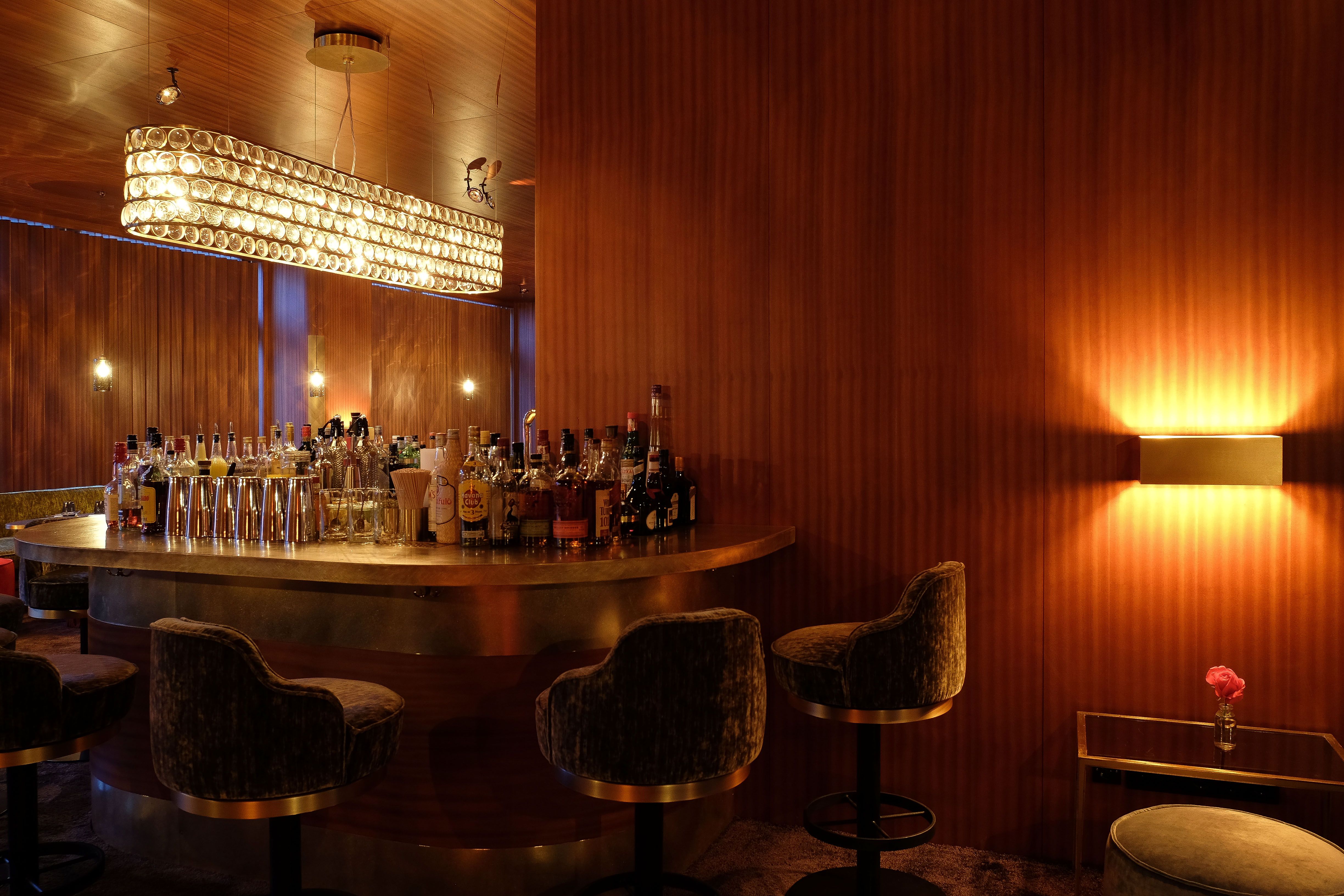 Die Barperspektive mit hinterleuchteten Spirituosen unterstreicht den hochwertigen Materialmix aus Metall, Holz und Stoff.