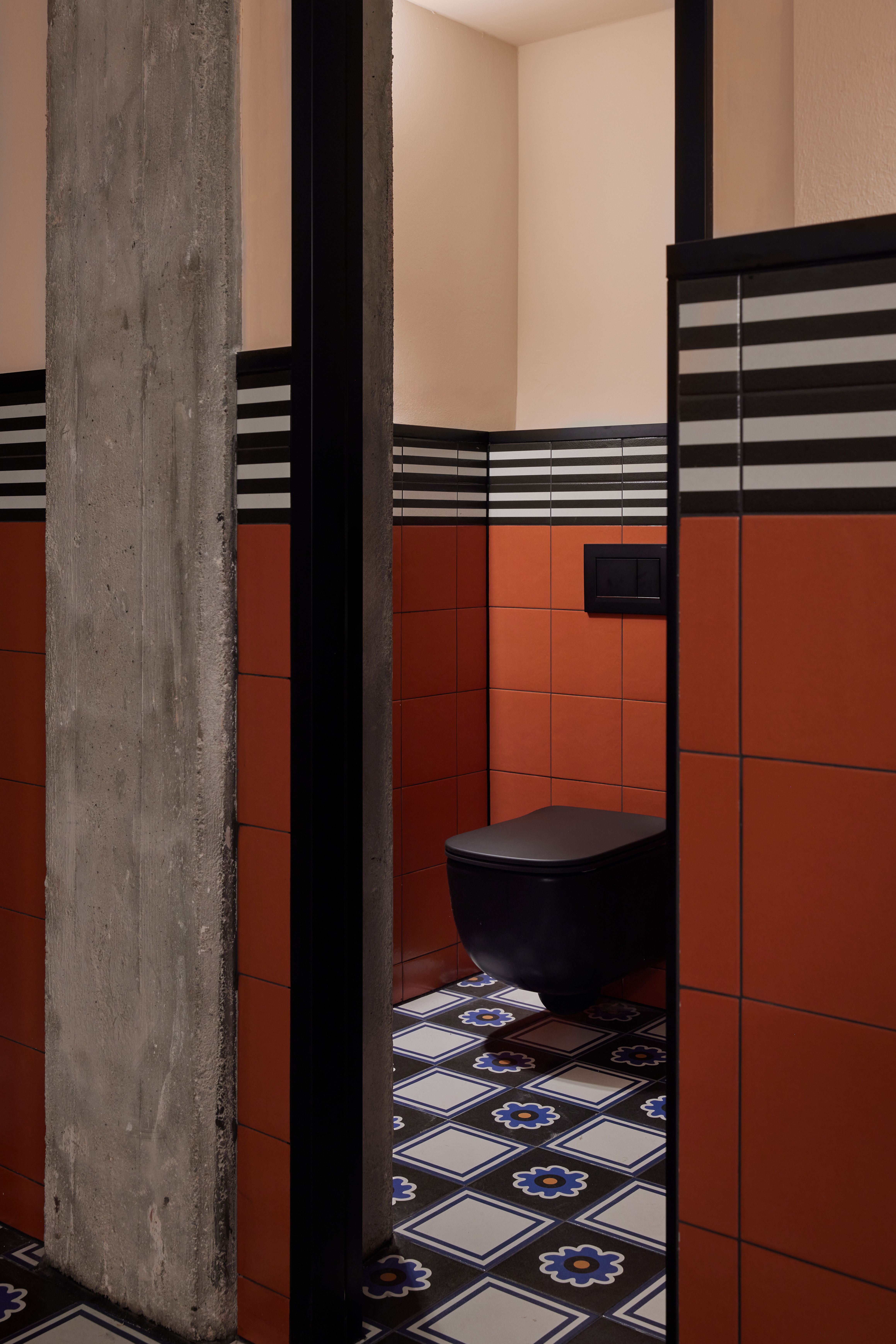 Die Sanitärkabine mit monochromem Black-Ceramic-WC, markanter Streifenfries-Fliese und roh belassenem Betonpfeiler wurde im Turbinenhaus Kolbermoor – Brasserie von Stephanie Thatenhorst designt.