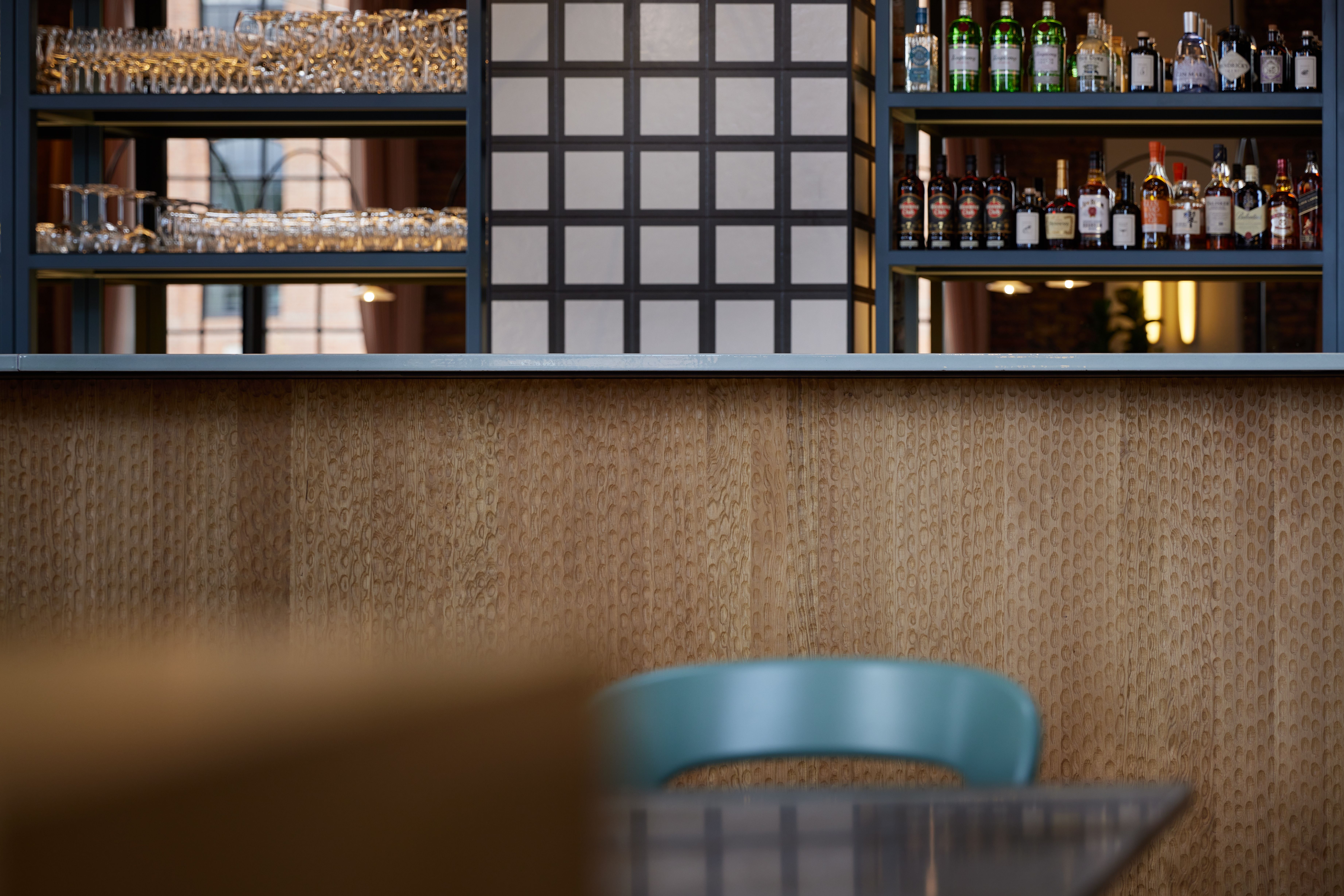 Die Barfront mit handgehobelter Holzoberfläche, modularem Stahl-Regalsystem und serieller Glasware-Präsentation wurde im Turbinenhaus Kolbermoor – Brasserie von Stephanie Thatenhorst designt.