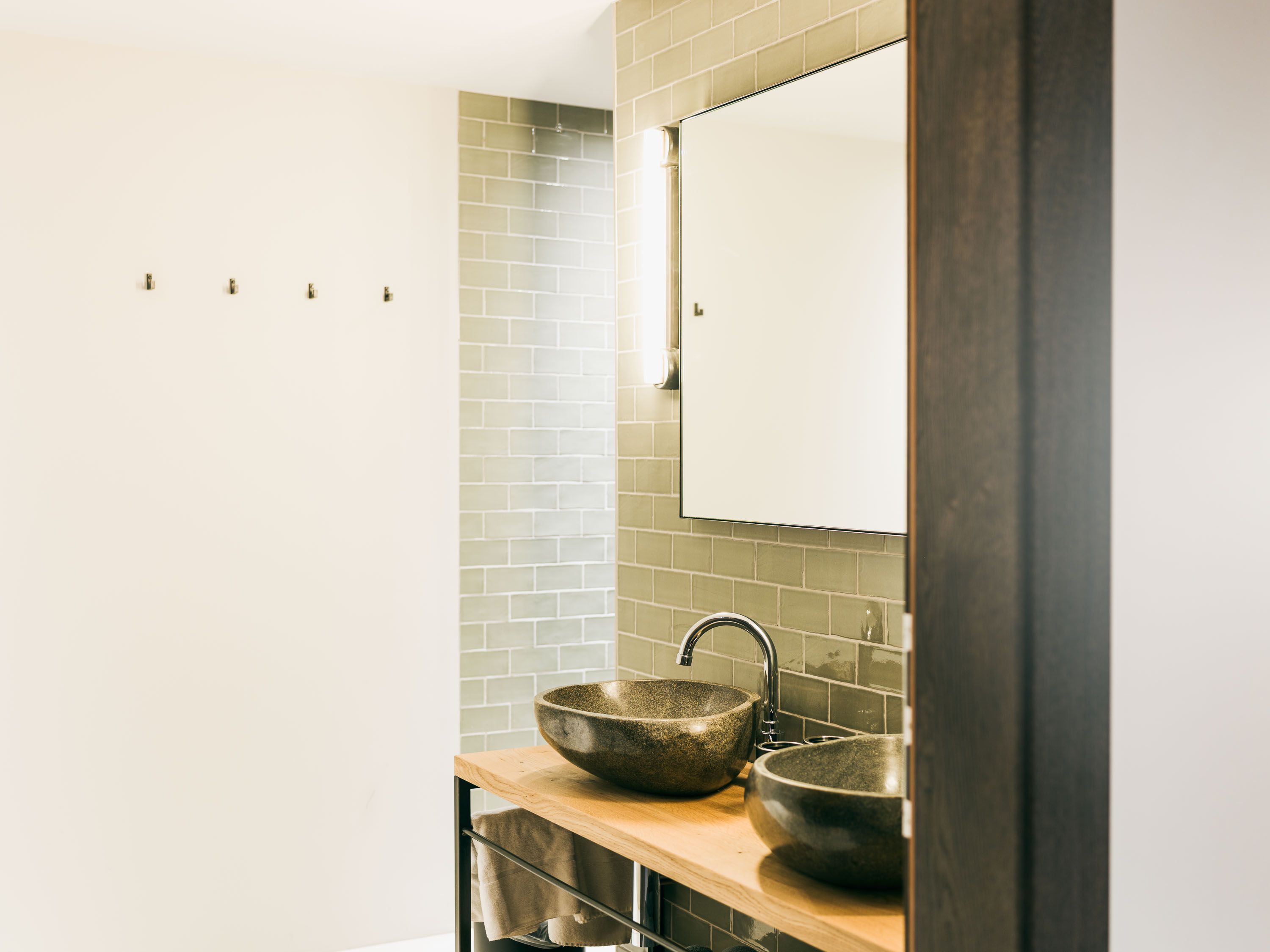 Das Badezimmer im Schönherrhaus Hotel überzeugt durch Natursteinwaschbecken, warme Holzdetails und klare Fliesenflächen, die zeitlose Eleganz mit hochwertigem Hotelkomfort verbinden.