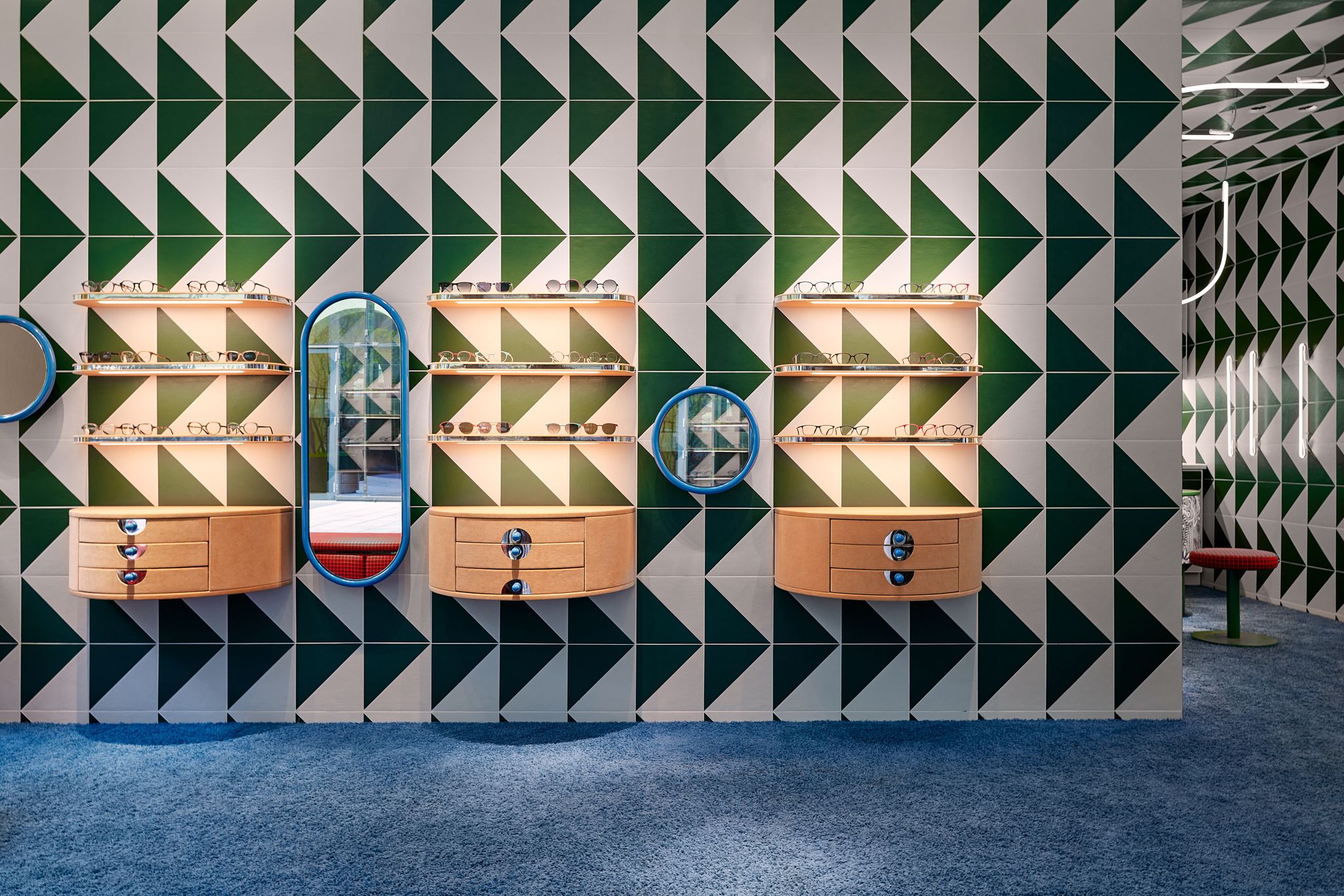 Die harmonisch beleuchtete Präsentationswand kombiniert symmetrische Brillenmodule mit farbstarker Musterkeramik und formt einen ikonischen Wiedererkennungswert – designt von Stephanie Thatenhorst für Rookies Eyewear for Kids.