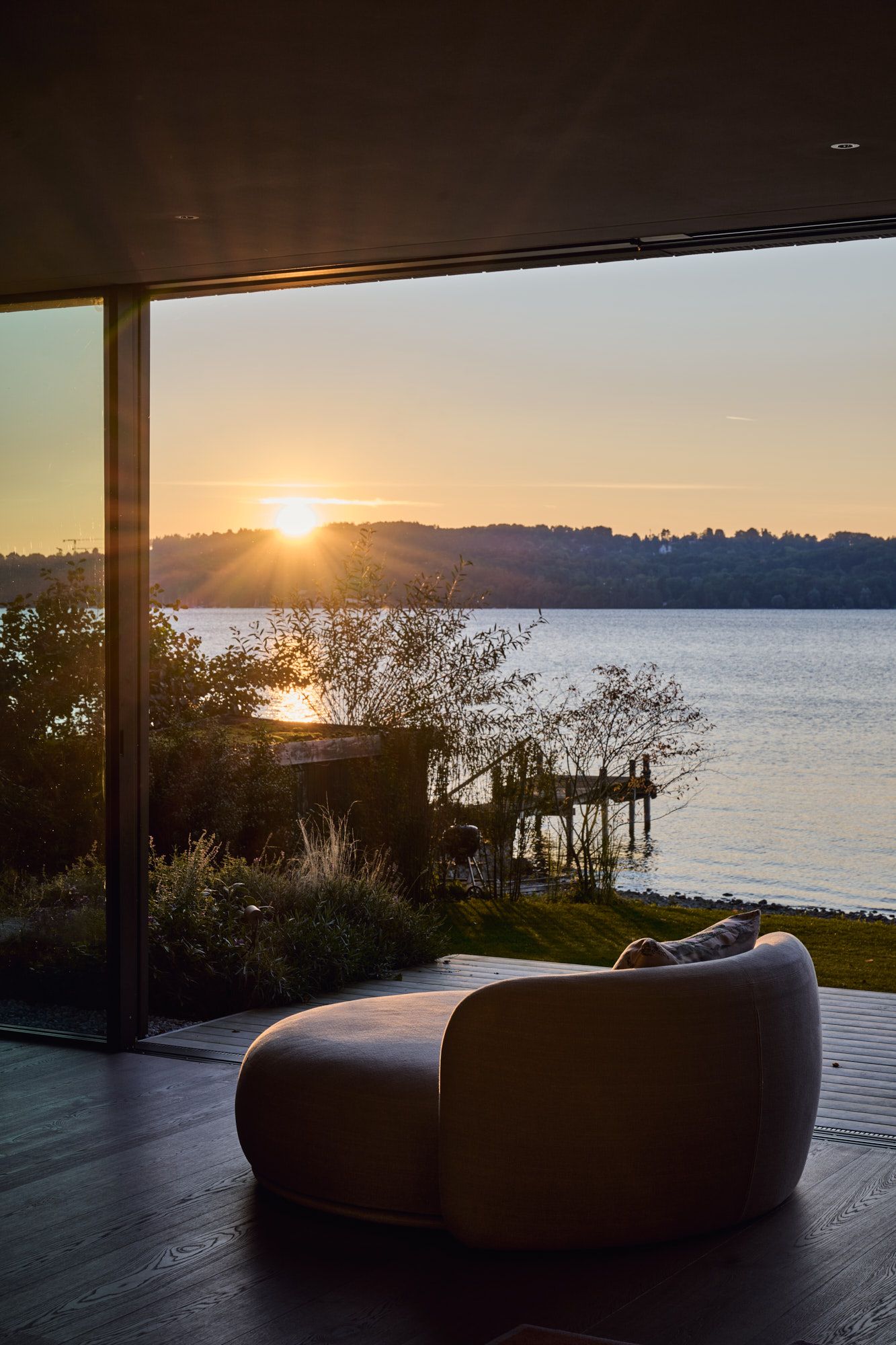 Ruhezone mit organischer Loungechair-Silhouette und eindrucksvollem Seeblick im warmen Abendlicht für ein atmosphärisch elegantes Wohnambiente.