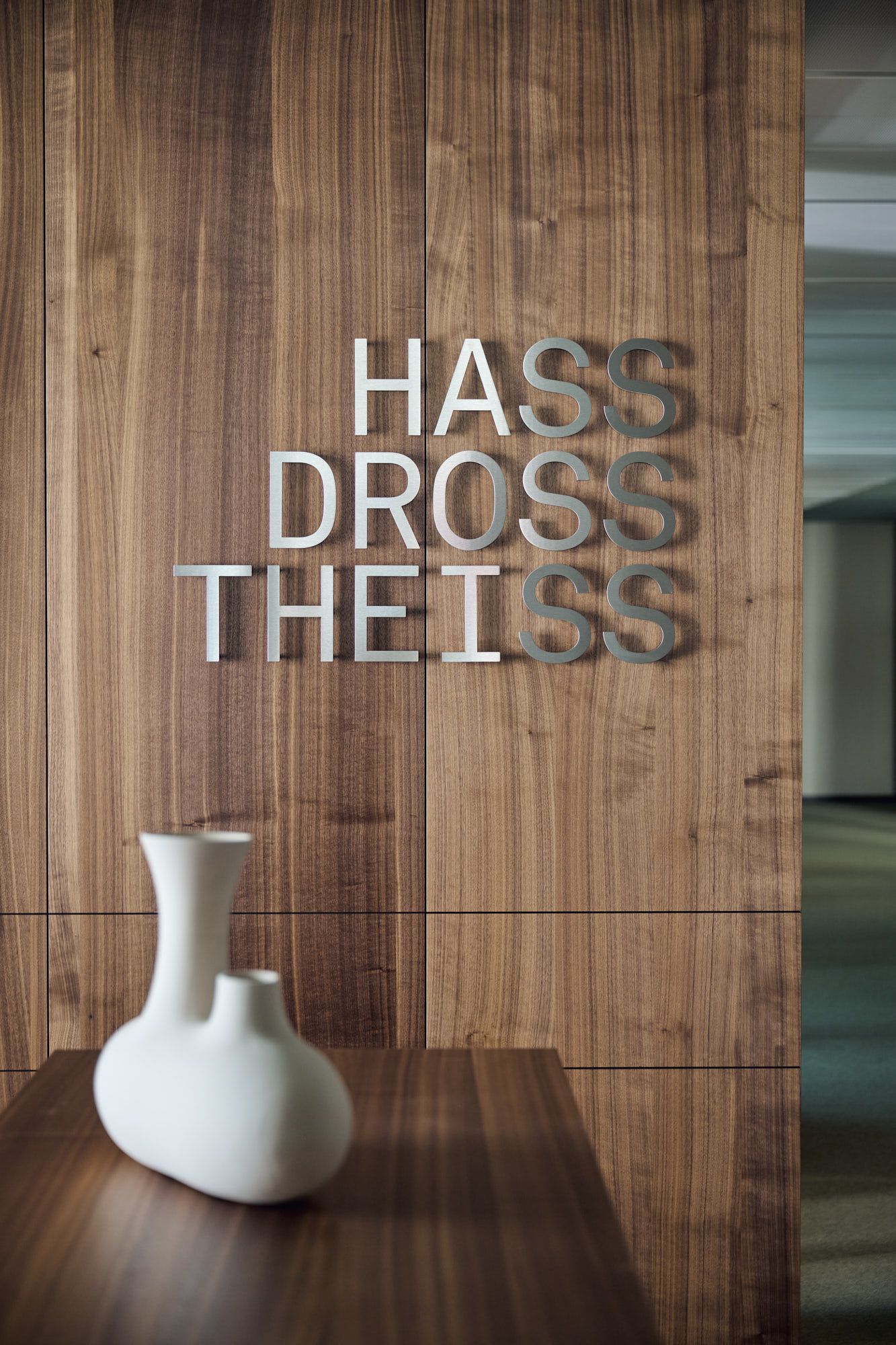 m Büro Hass Dross Theiss setzt Stephanie Thatenhorst auf klare Typografie, warmes Holz und subtile Objektakzente, um einen modernen und zugleich einladenden Empfangsbereich zu gestalten.“
