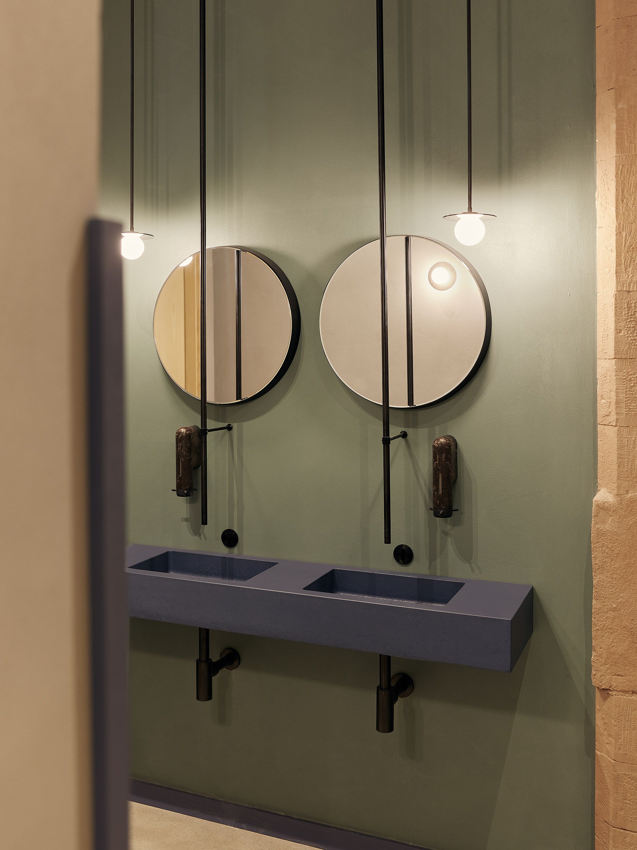 Die blau akzentuierte Waschtischanlage mit filigranen Hängeleuchten zeigt die hochwertige, grafische Gestaltung des Sanitärbereichs im Benediktiner Weissbräuhaus.