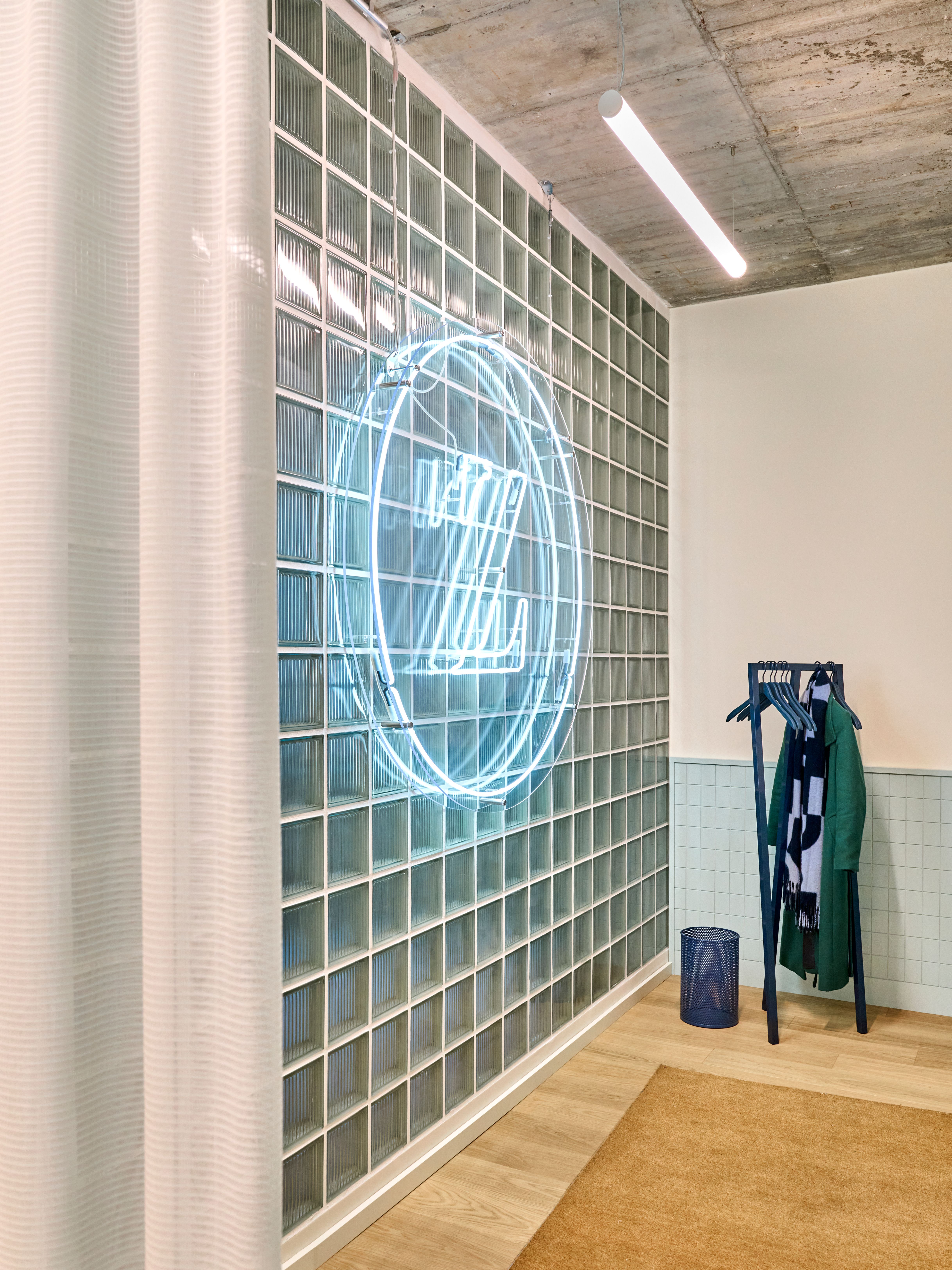 Eine gläserne Wand mit leuchtendem Neonlogo setzt ein modernes, urbanes Statement im Empfangsbereich der von Stephanie Thatenhorst entworfenen Zahnarztpraxis „Lieblingszahnarzt“.