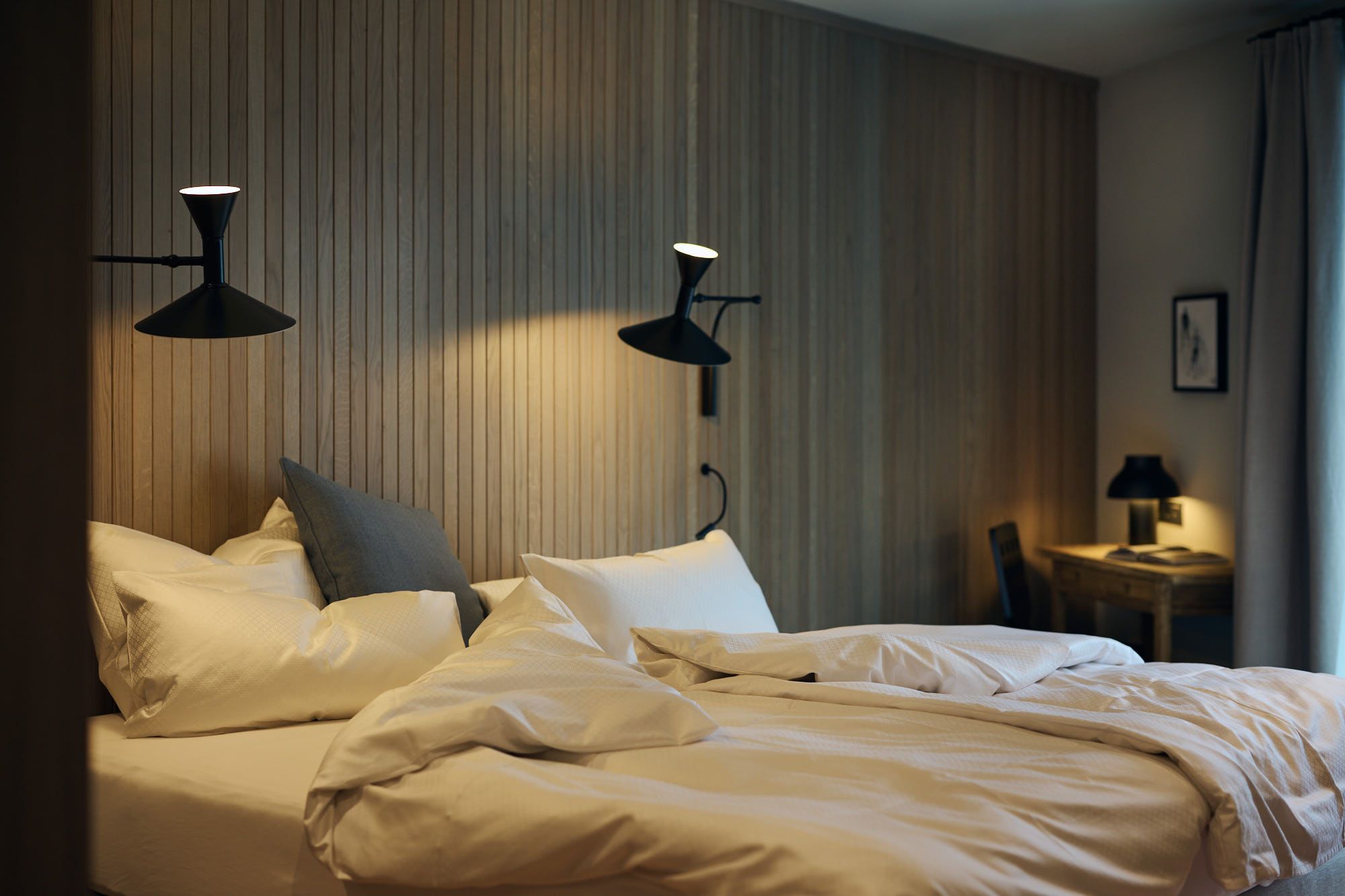 Das Schlafzimmer im Ullrhaus – gestaltet von Stephanie Thatenhorst – kombiniert warme Holzvertäfelung und ikonische Wandlampen zu einer ruhigen, zeitlosen Atmosphäre.