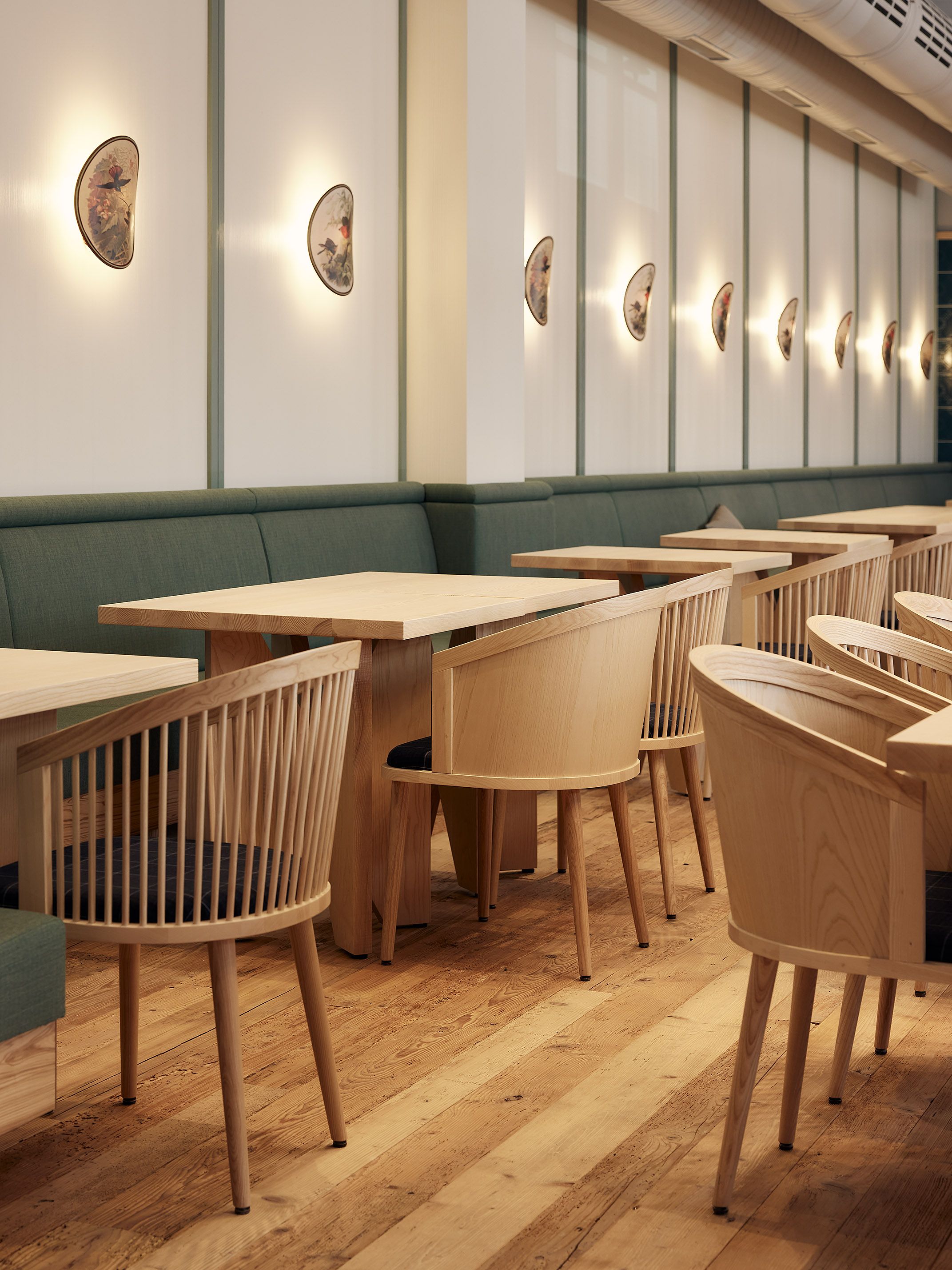 Helle Holztische und grüne Polsterbänke formen die einladende Sitzlandschaft des Benediktiner Weissbräuhaus mit typischer Thatenhorst-Detailpräzision.