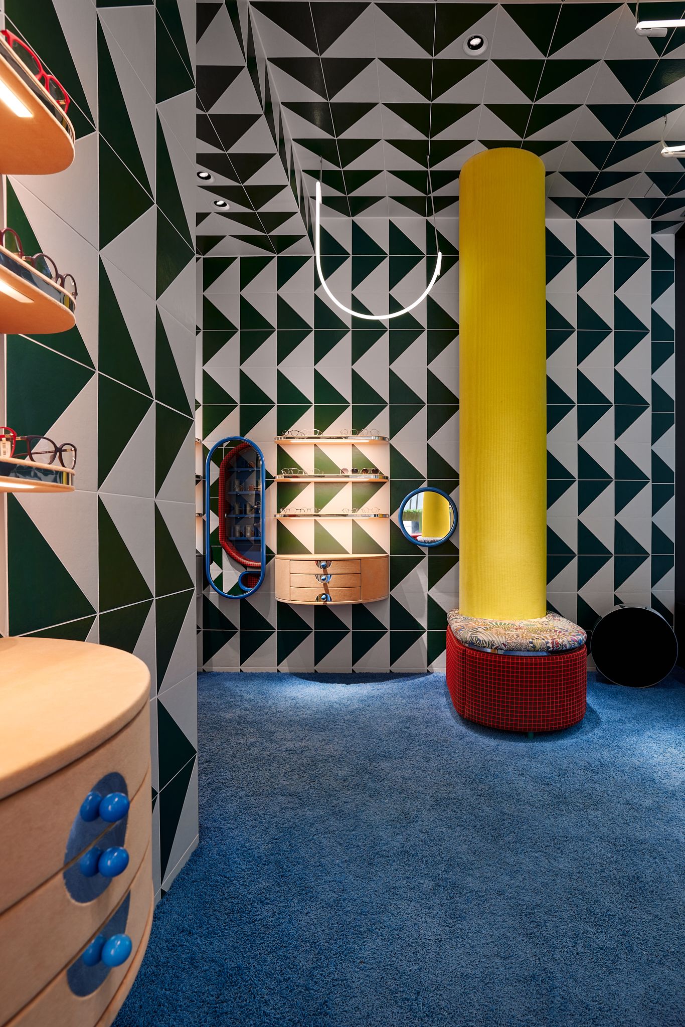 Der Raum zeigt ein intensives Zusammenspiel aus farbigen Fliesen, markanten Rundspiegeln und leuchtenden Designlampen, die die Kinderbrillen wirkungsvoll inszenieren – designt von Stephanie Thatenhorst für Rookies Eyewear for Kids.